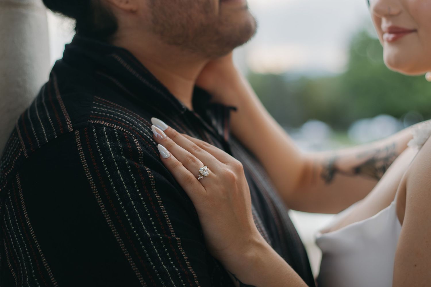 Intimate close-up of a couple embracing, with hands resting on a black striped shirt.