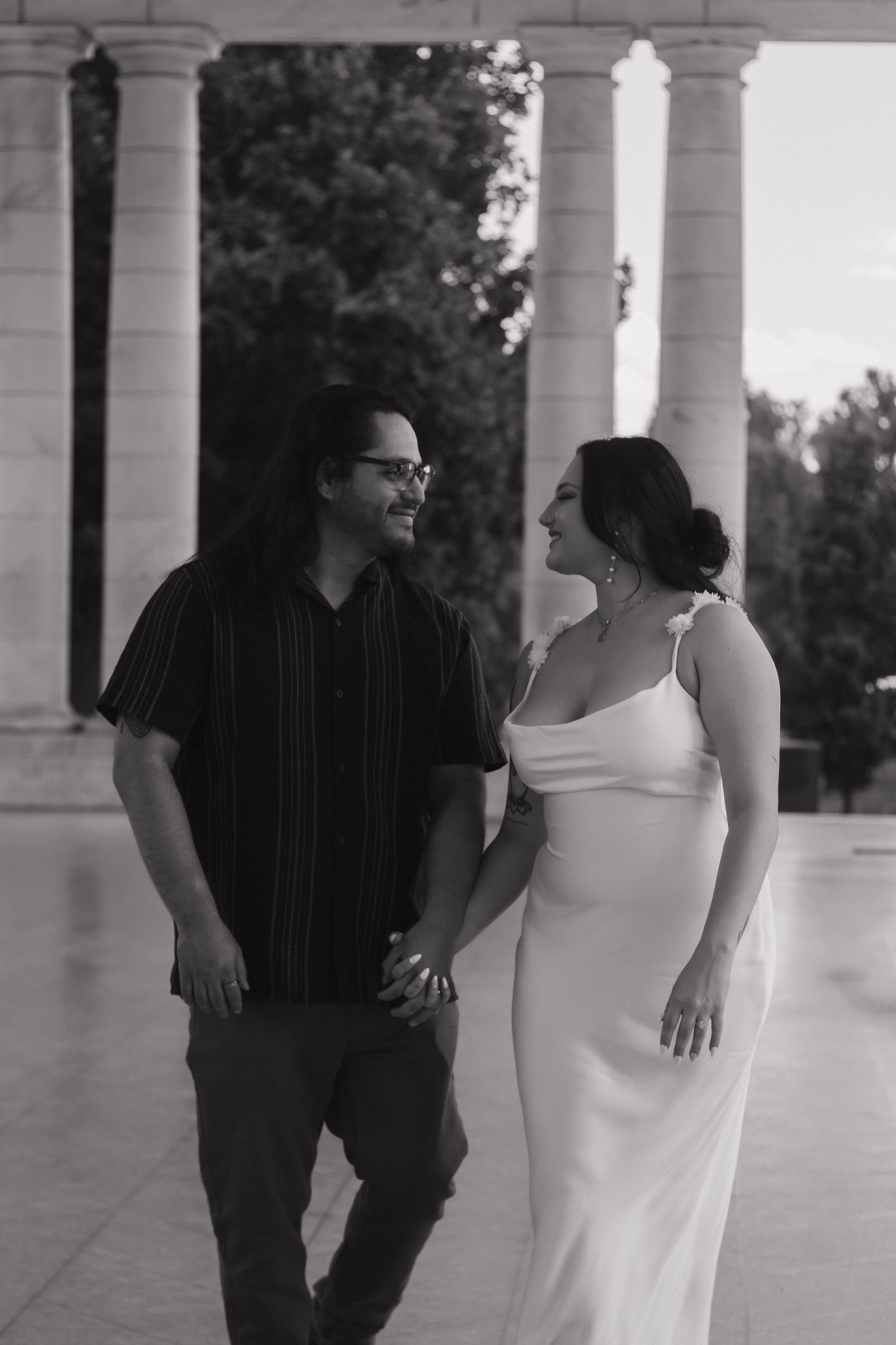 A couple shares a tender moment under white classical columns during a photo shoot.