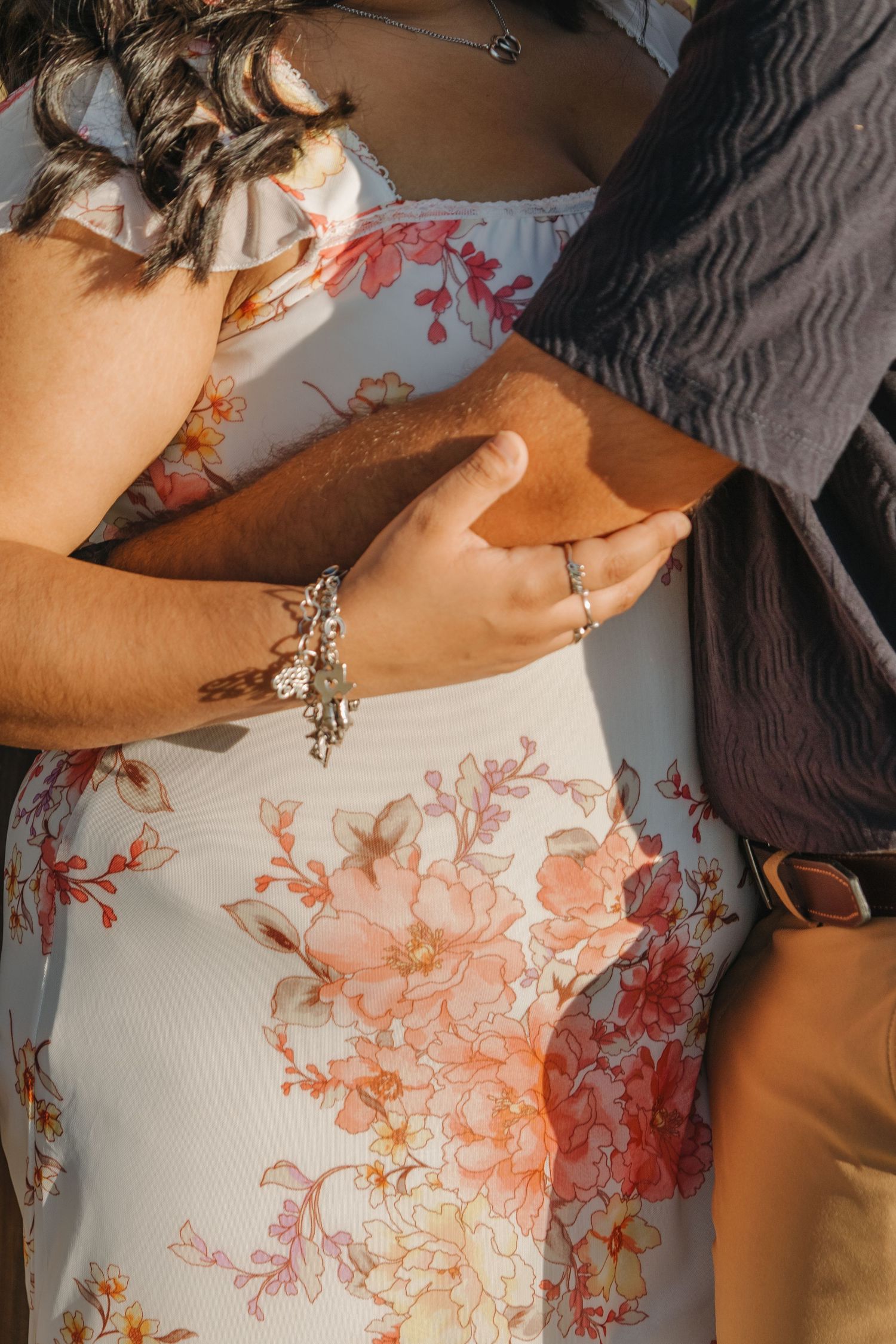 Close-up of hands wearing rings and bracelets against a floral patterned dress.