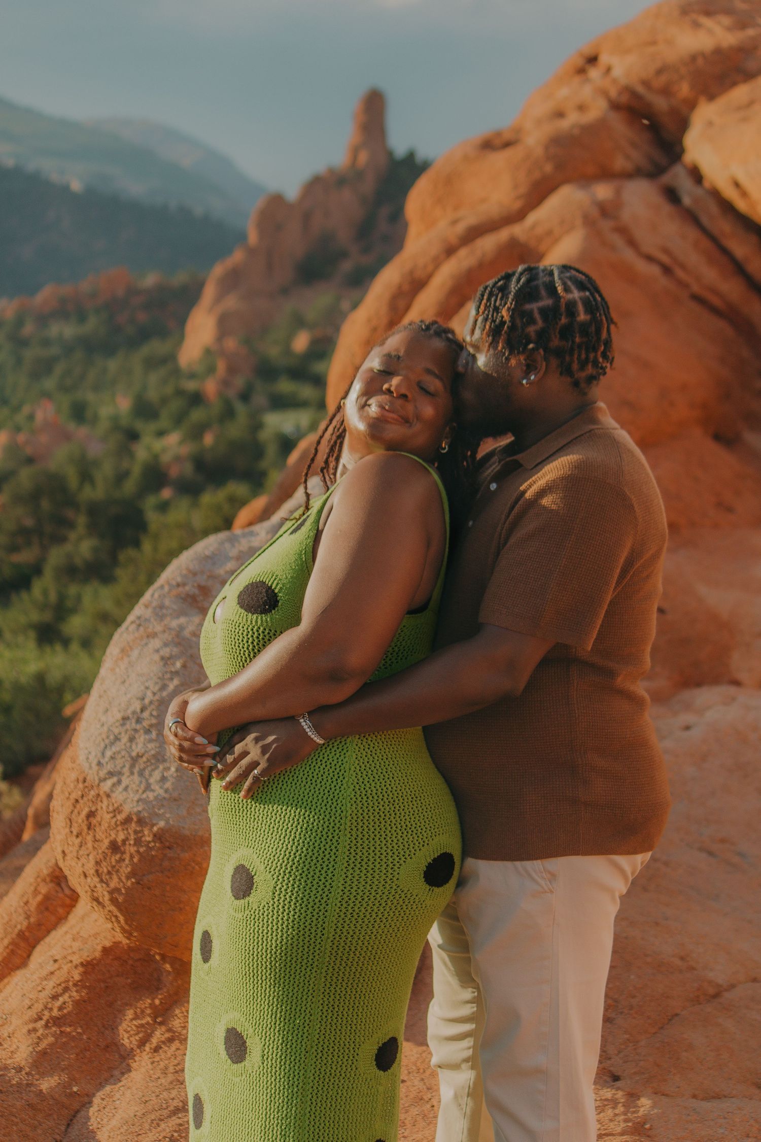 Two people share a tender moment against red rock formations at sunset.