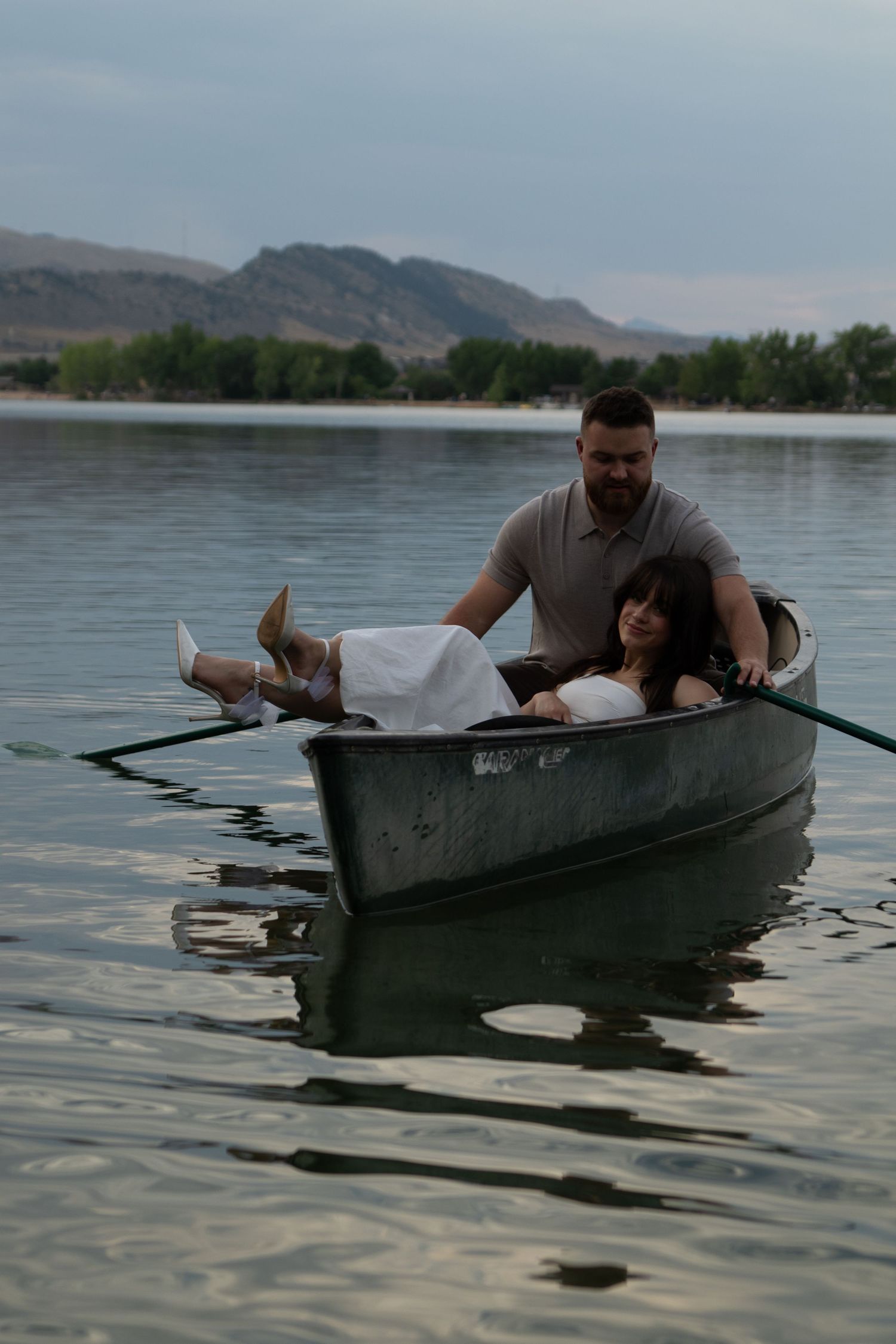A couple enjoying a tranquil boat ride on a lake surrounded by mountain landscapes.