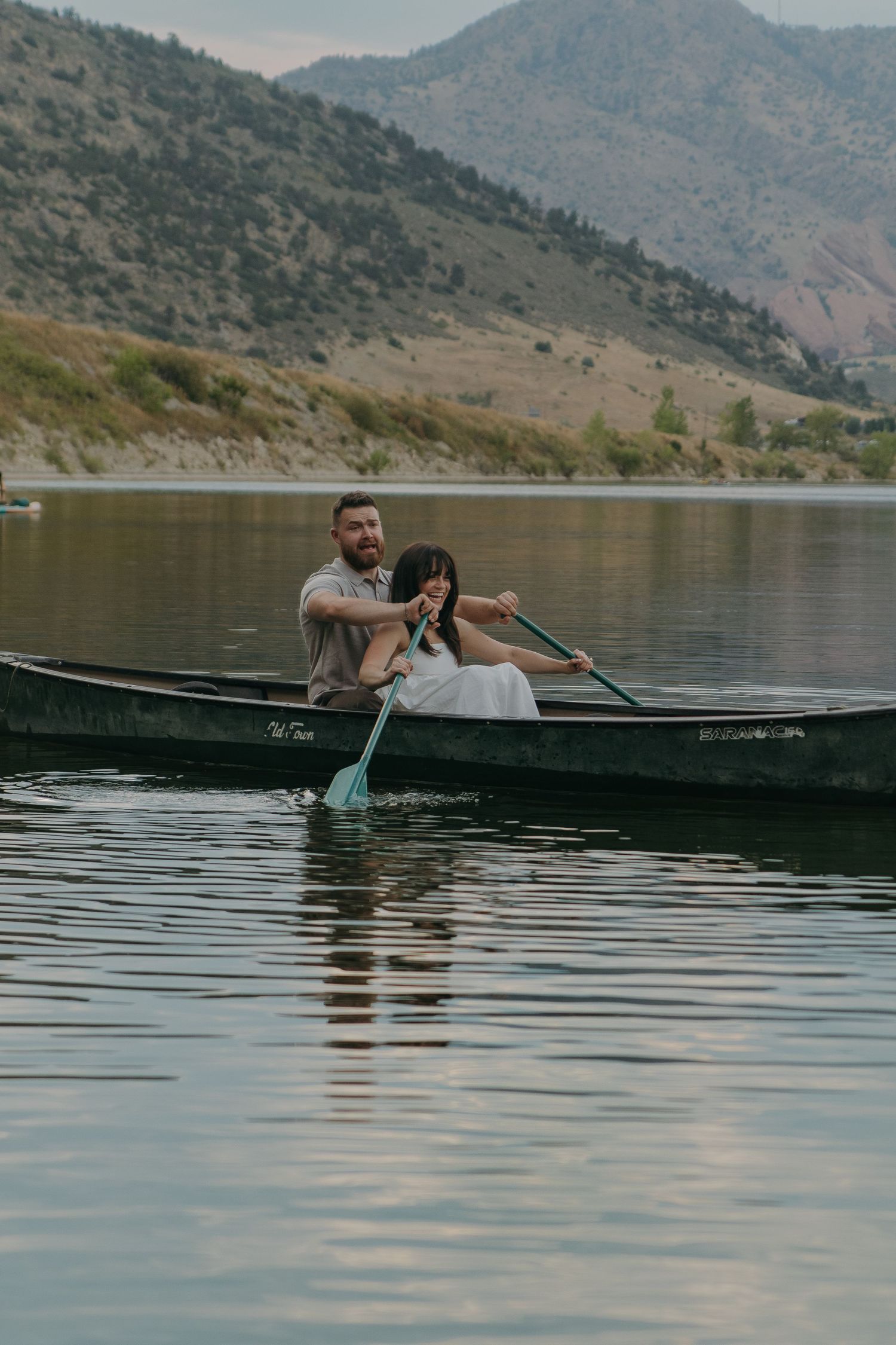 A couple sits romantically in a canoe on a serene mountain lake surrounded by hills.