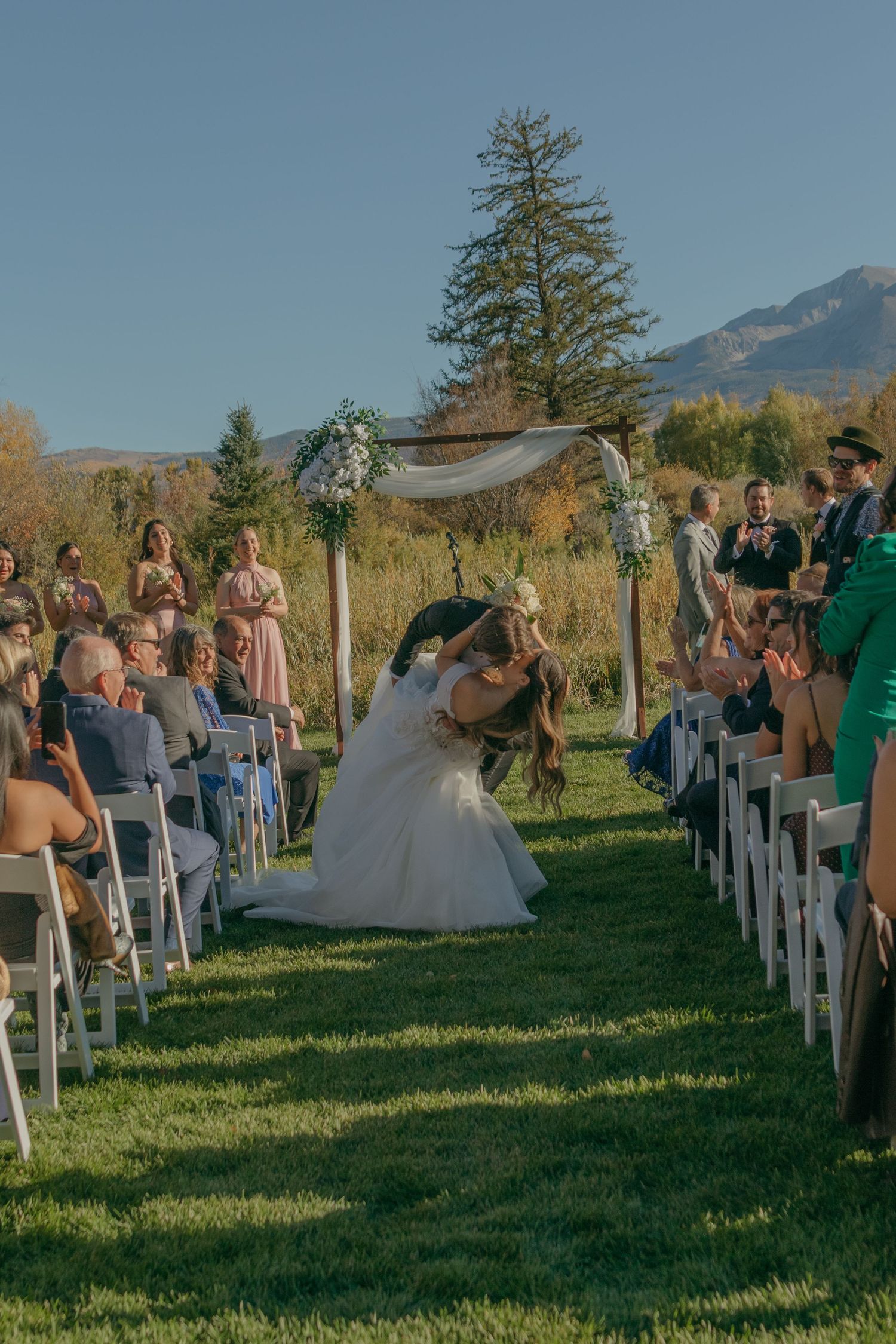 Outdoor wedding ceremony setup with white chairs and mountain views in the background.