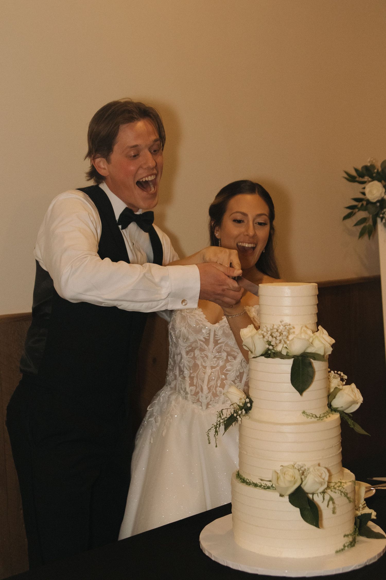 A couple cuts and feeds each other bites of their elegant white tiered wedding cake.
