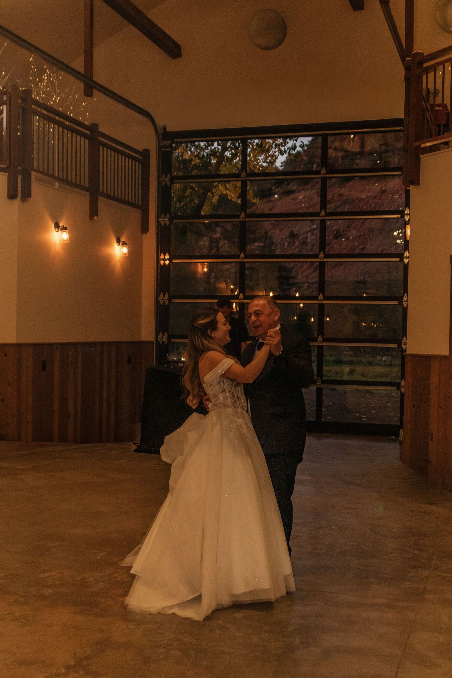 Couple sharing their first dance in an elegant reception hall with large windows.