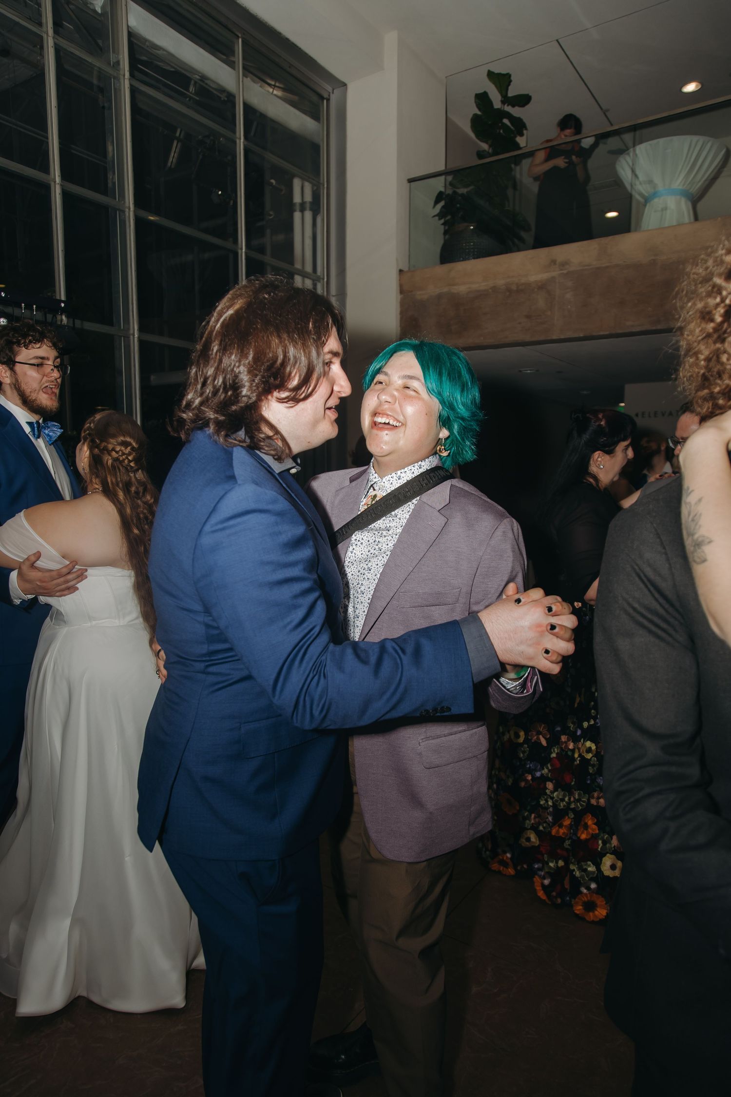 Two guests in suits laugh and dance joyfully together at a lively indoor wedding reception celebration.