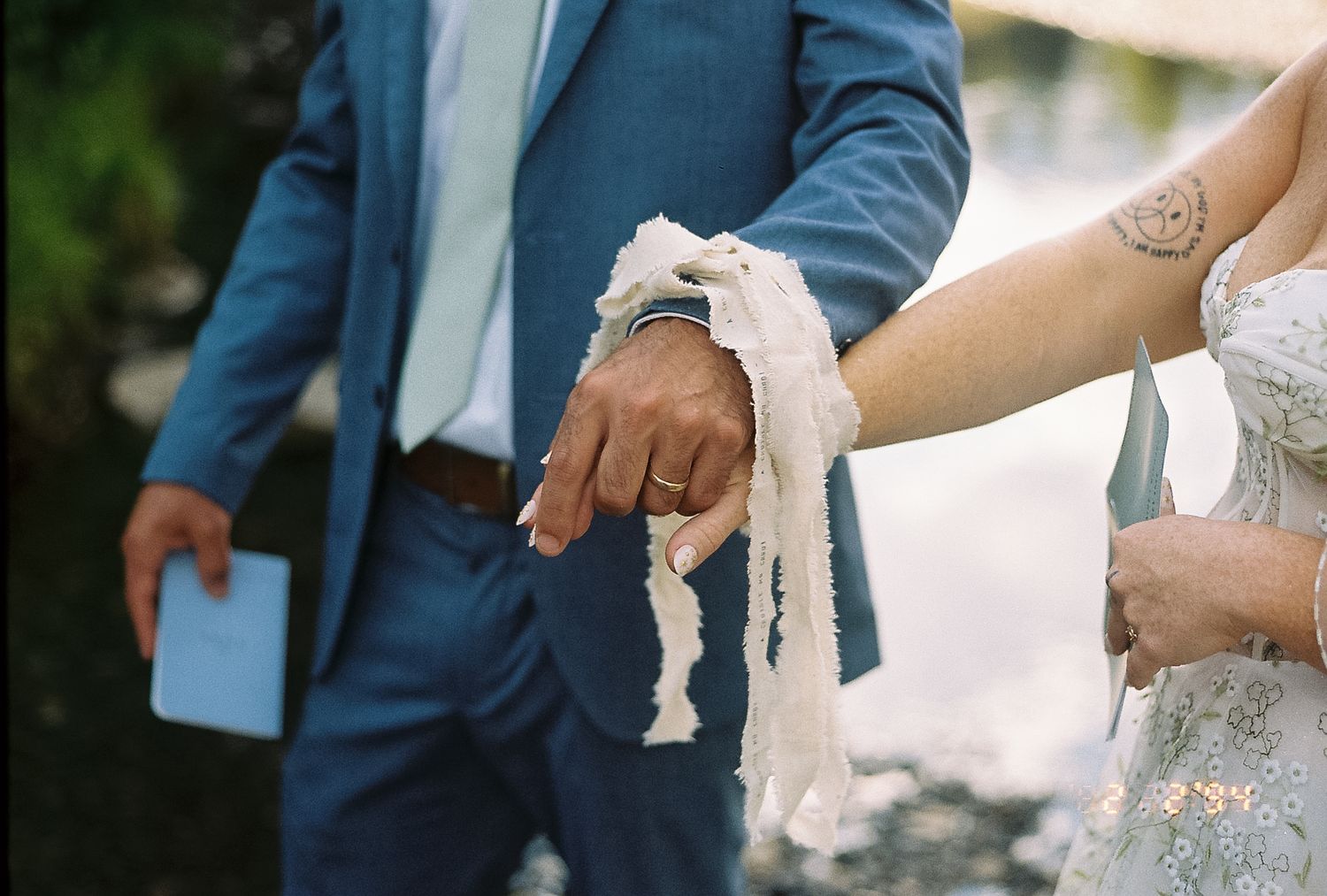 Close-up of groom's hand bound with white ribbon during outdoor wedding handfasting ceremony.