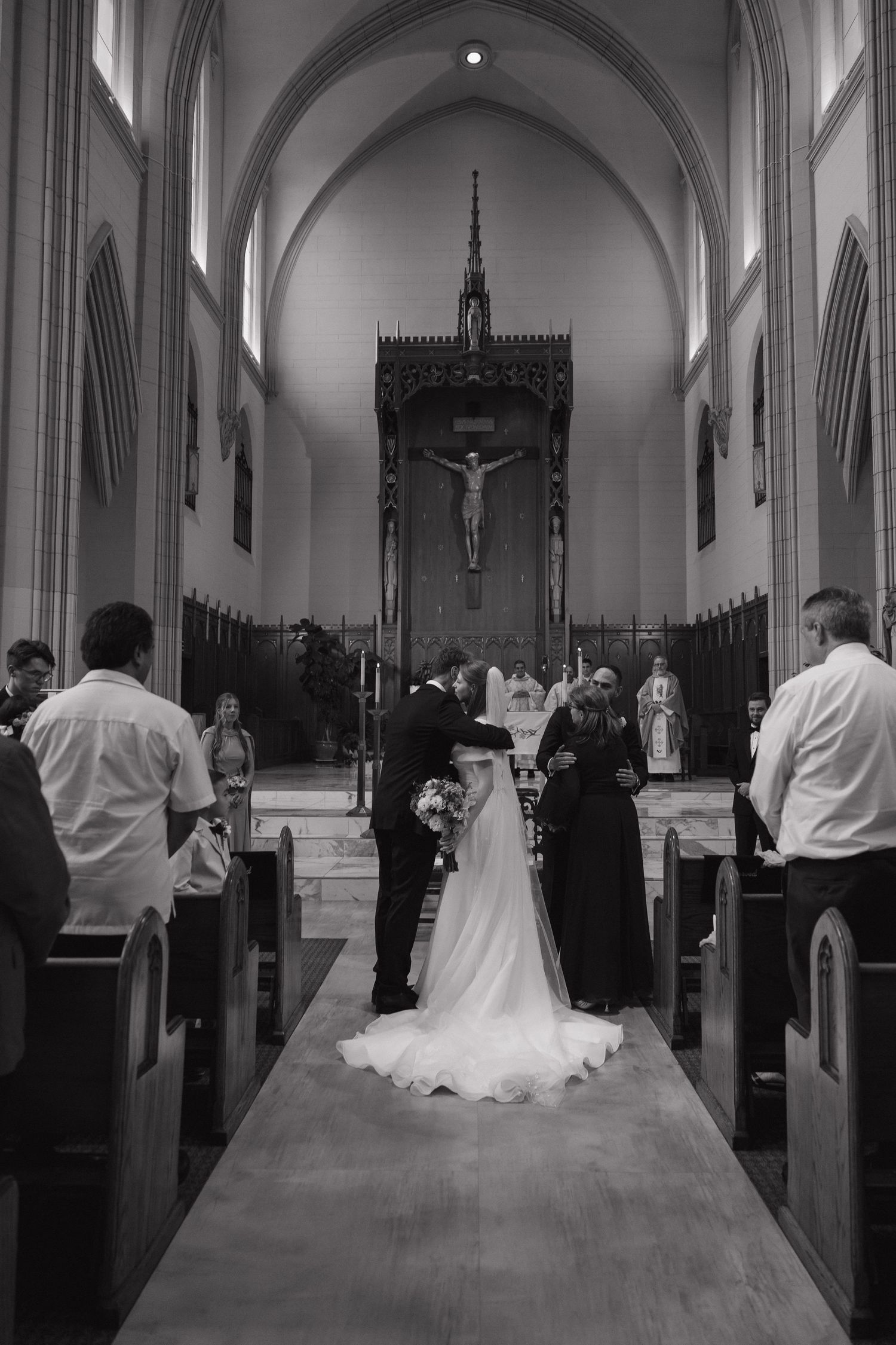 Black and white photo of bride and groom walking down church aisle toward crucifix altar during wedding ceremony.