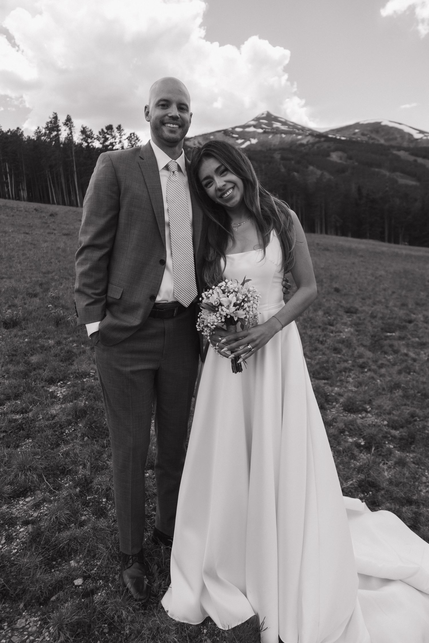 Black and white portrait of smiling bride and groom posing in a mountain meadow on wedding day.