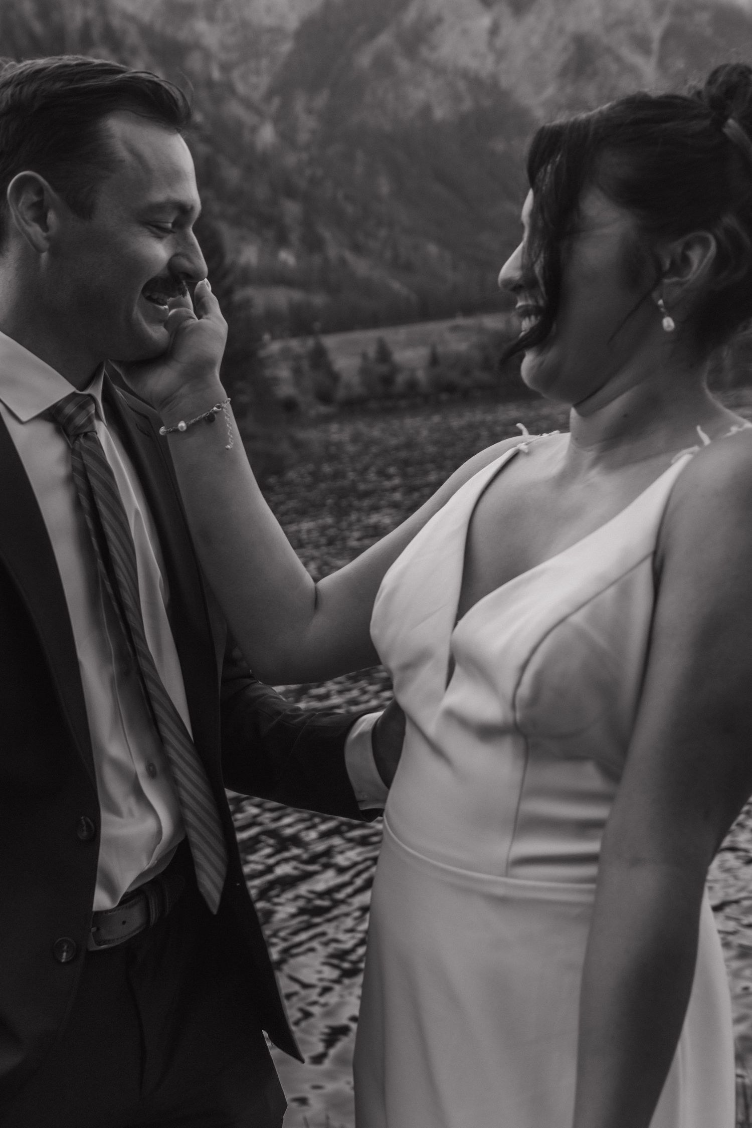 A candid black and white moment between two people during a lakeside mountain wedding ceremony.