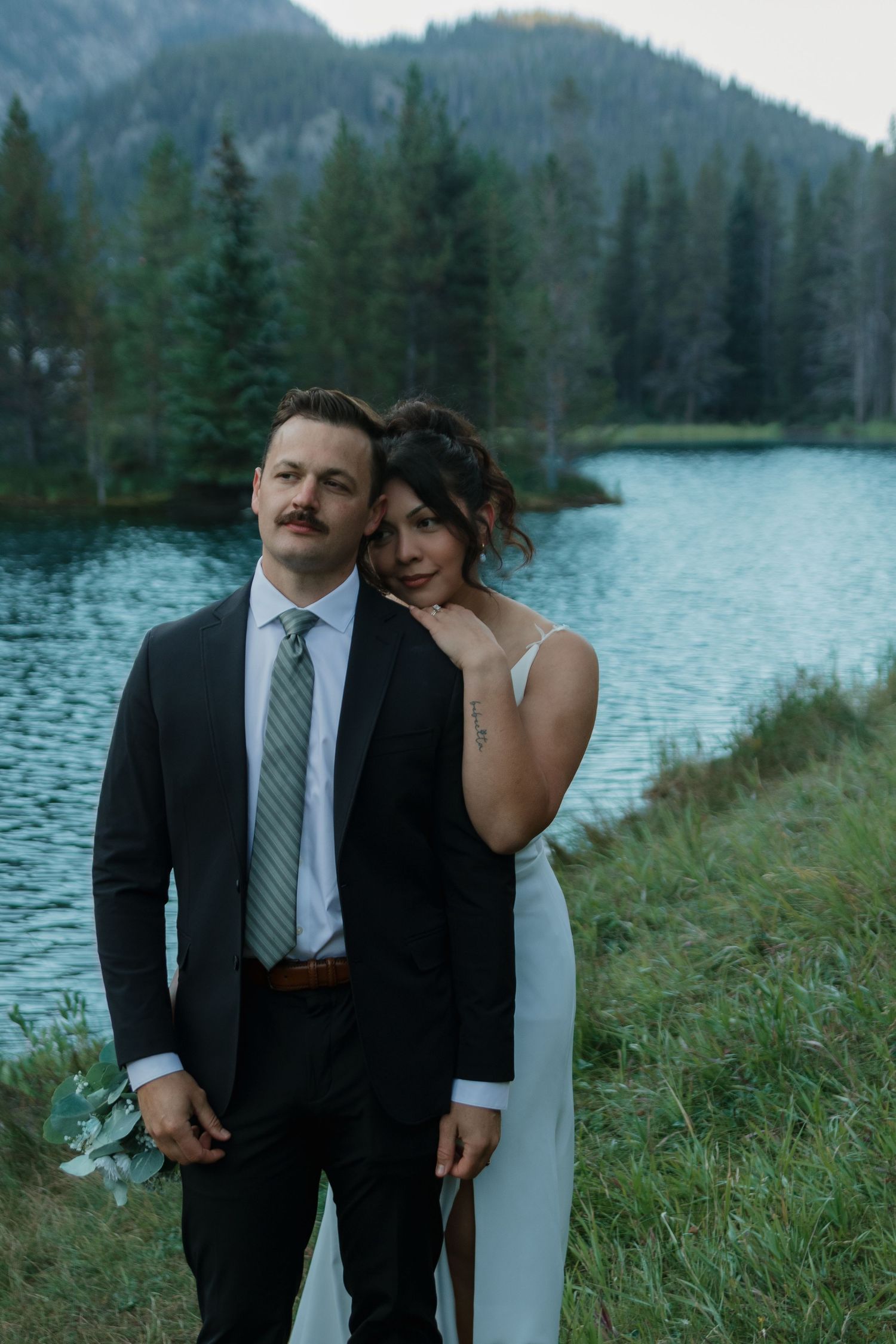 A wedding couple poses together against a scenic mountain lake landscape.
