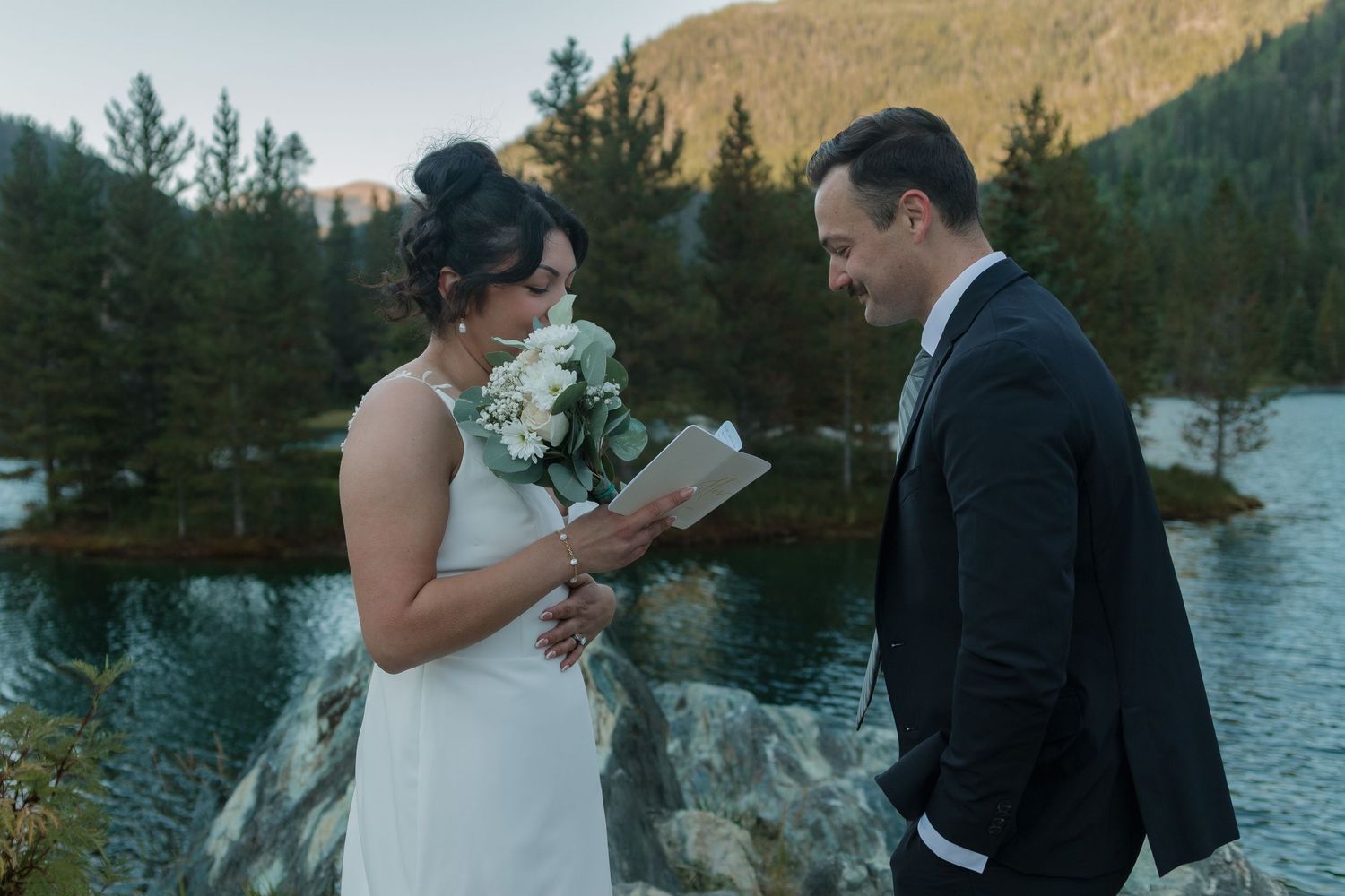 A wedding ceremony at dusk with a mountain lake backdrop as vows are exchanged.