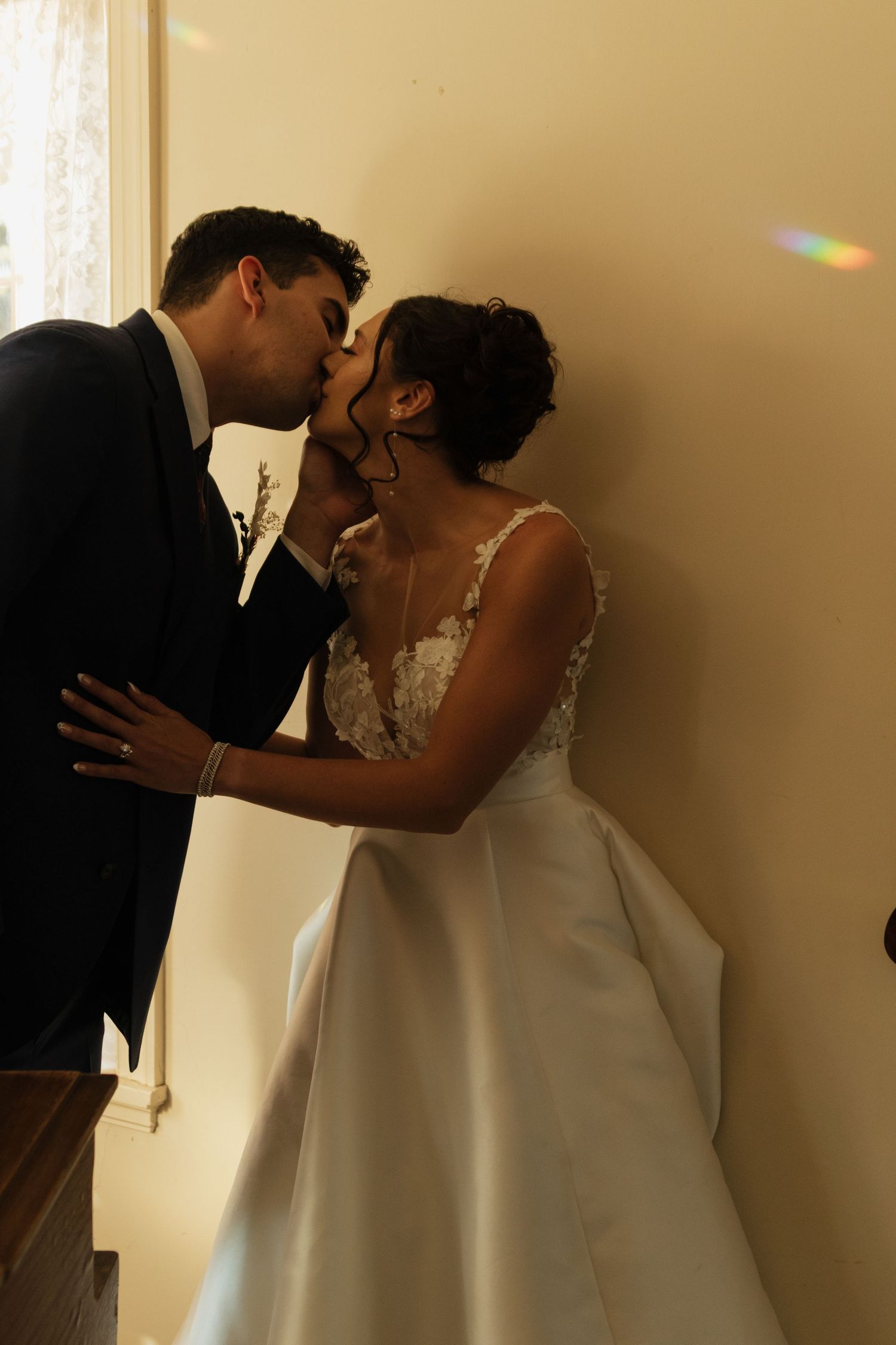 Romantic wedding moment captured in soft lighting against a wall.