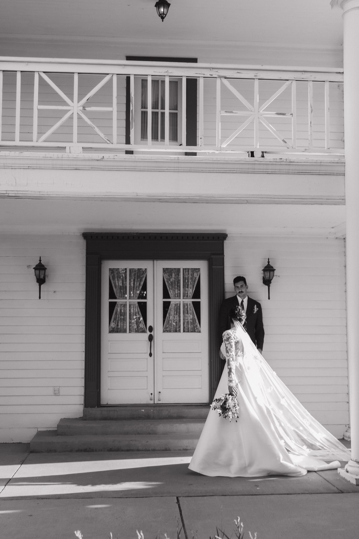 Dramatic bridal portraits showing flowing train against white colonial-style building architecture.