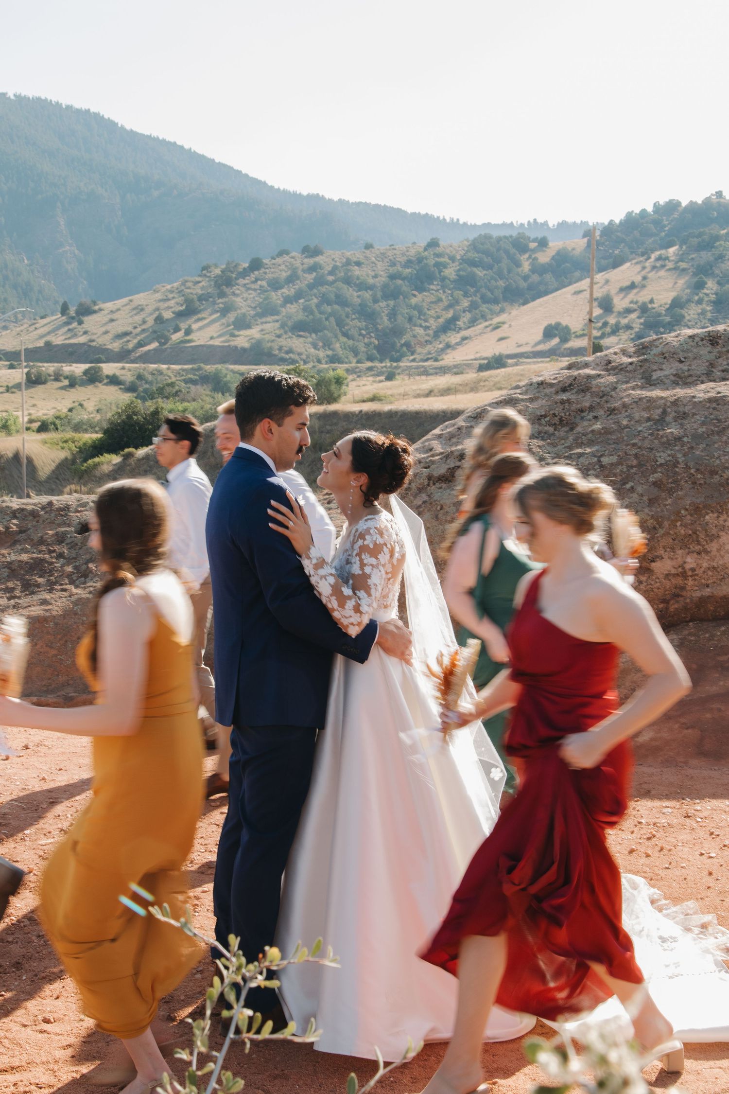 Wedding party members dance and celebrate against a mountainous desert landscape.
