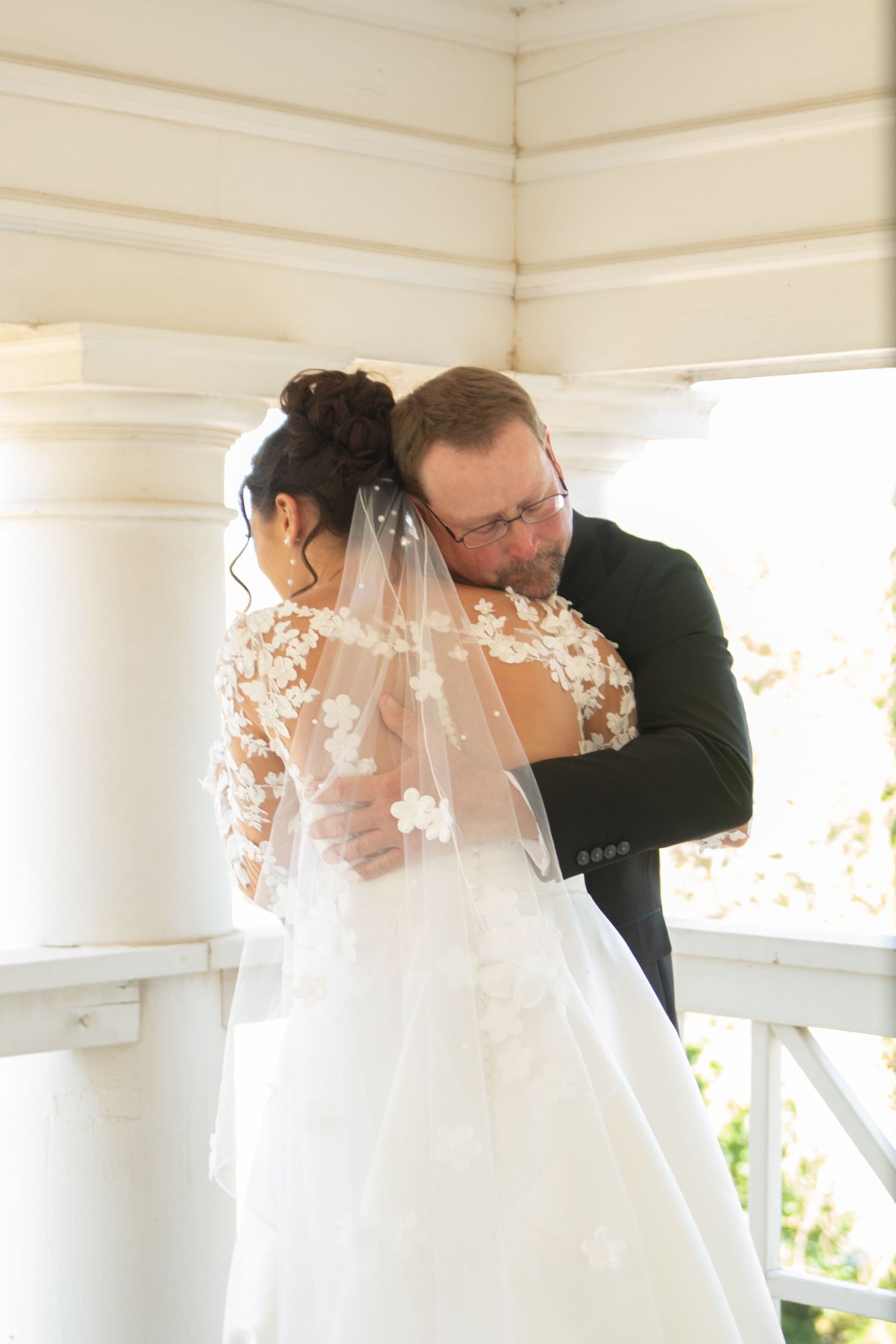 Emotional first look moment captured on a sunlit white porch.