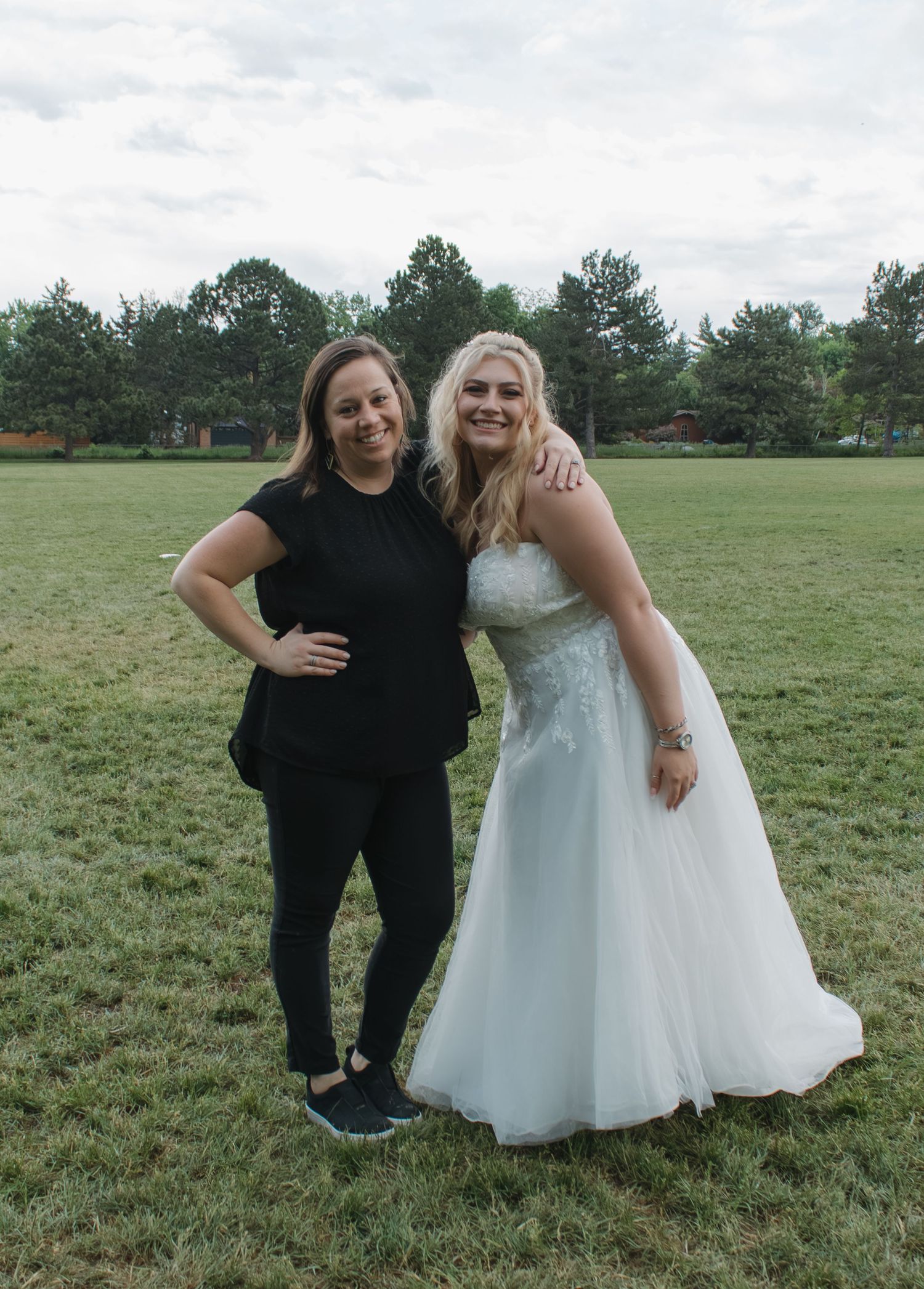 Wedding photo of two people embracing on grassy field with trees in background.