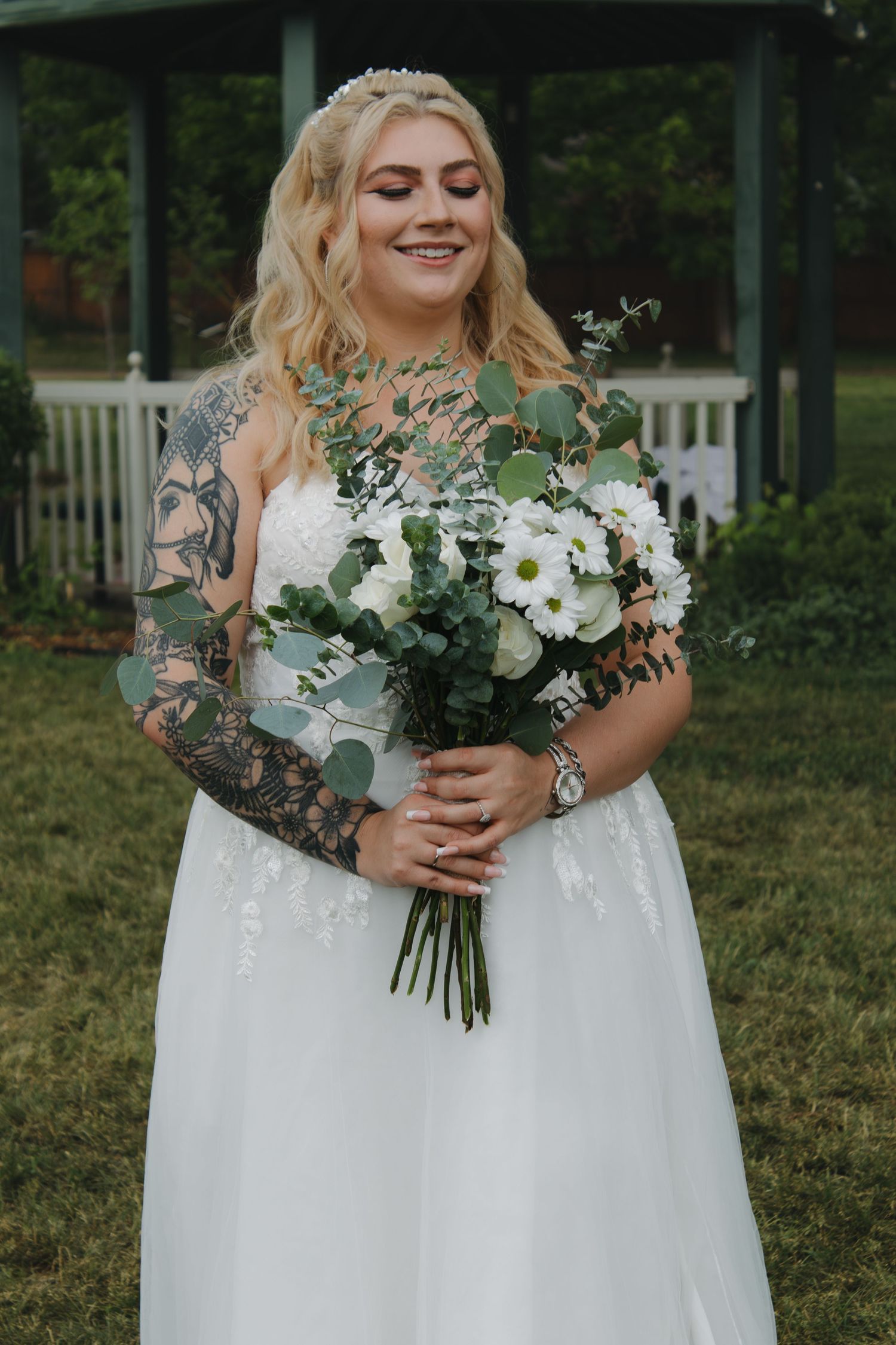 Elegant white wedding bouquet held against flowing lace bridal gown outdoors.