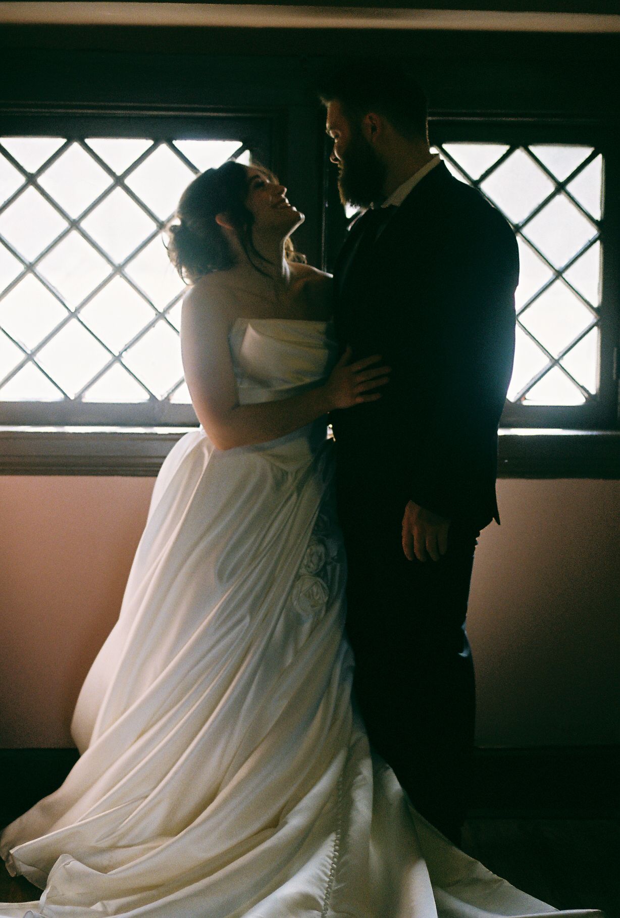Wedding couple dancing in an intimate indoor setting with window light.