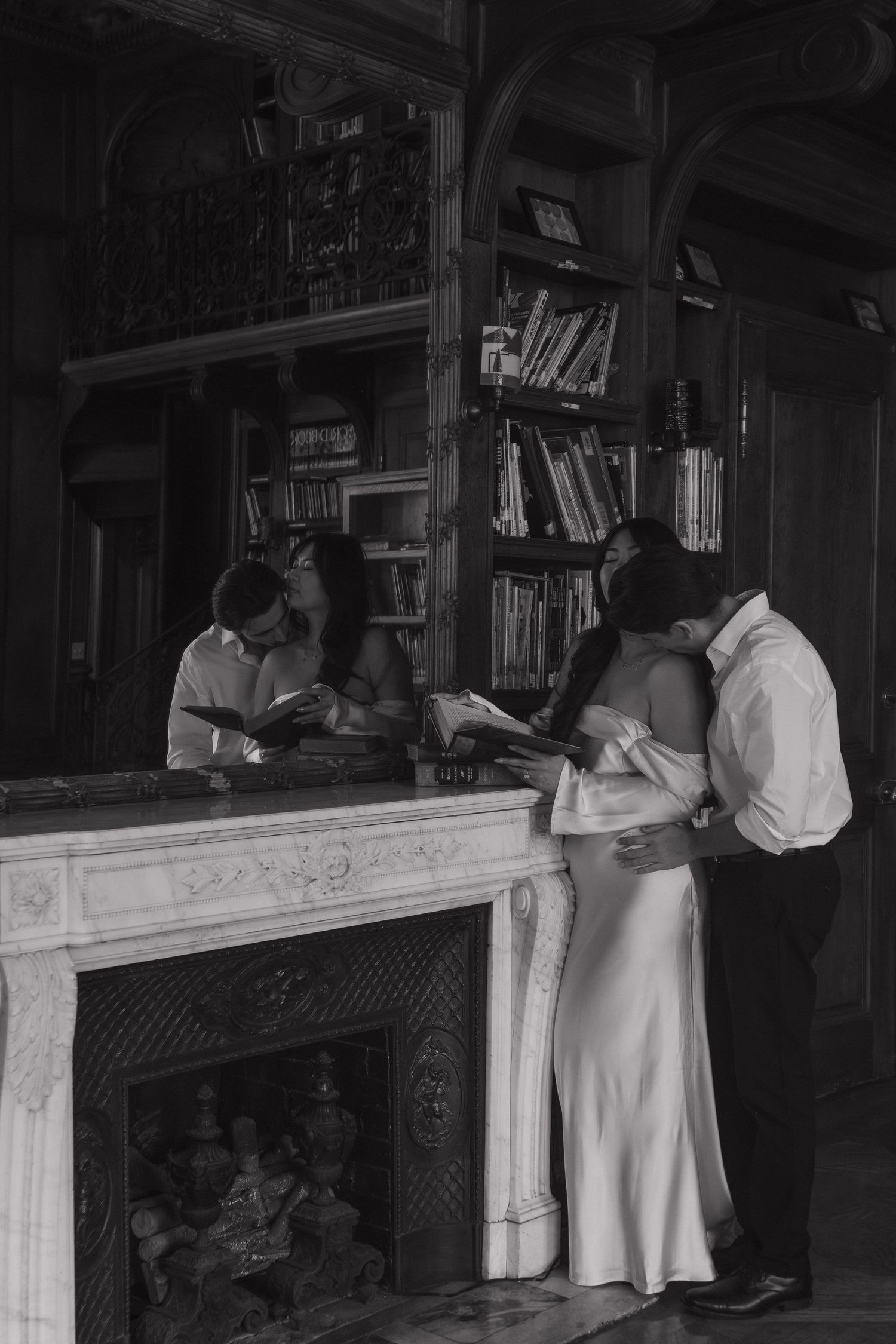 A couple in vintage attire shares an intimate moment by a fireplace with bookshelves in an elegant library setting.
