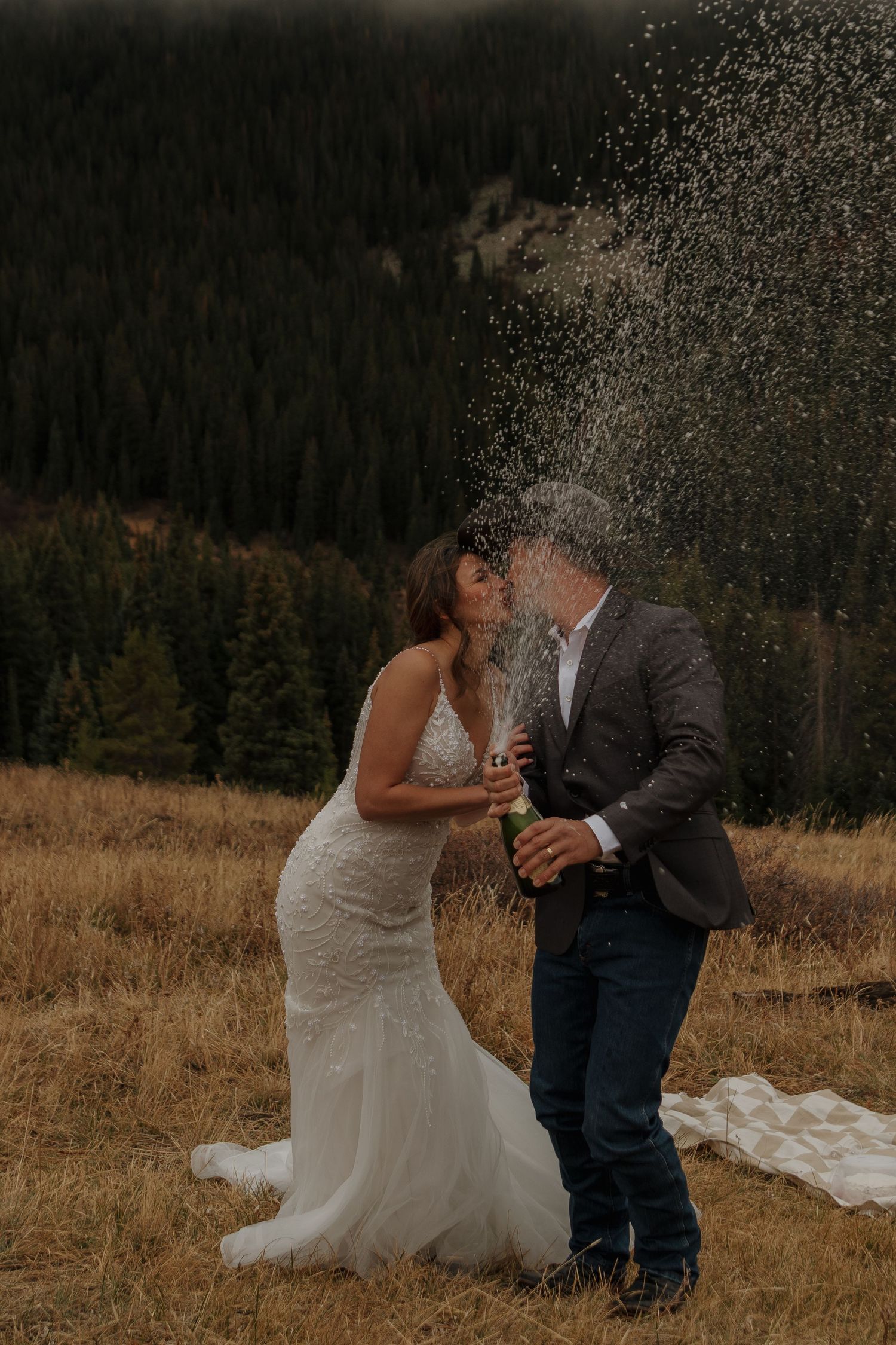 A couple celebrates with champagne spray on a mountainside during their wedding.
