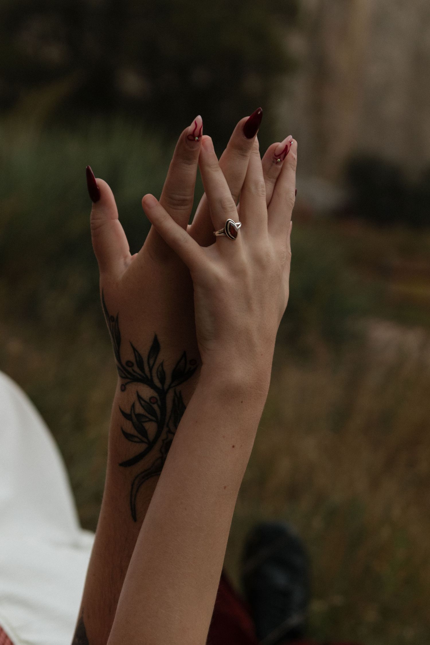 A hand displays a black tree silhouette tattoo on the forearm against a blurred outdoor background.