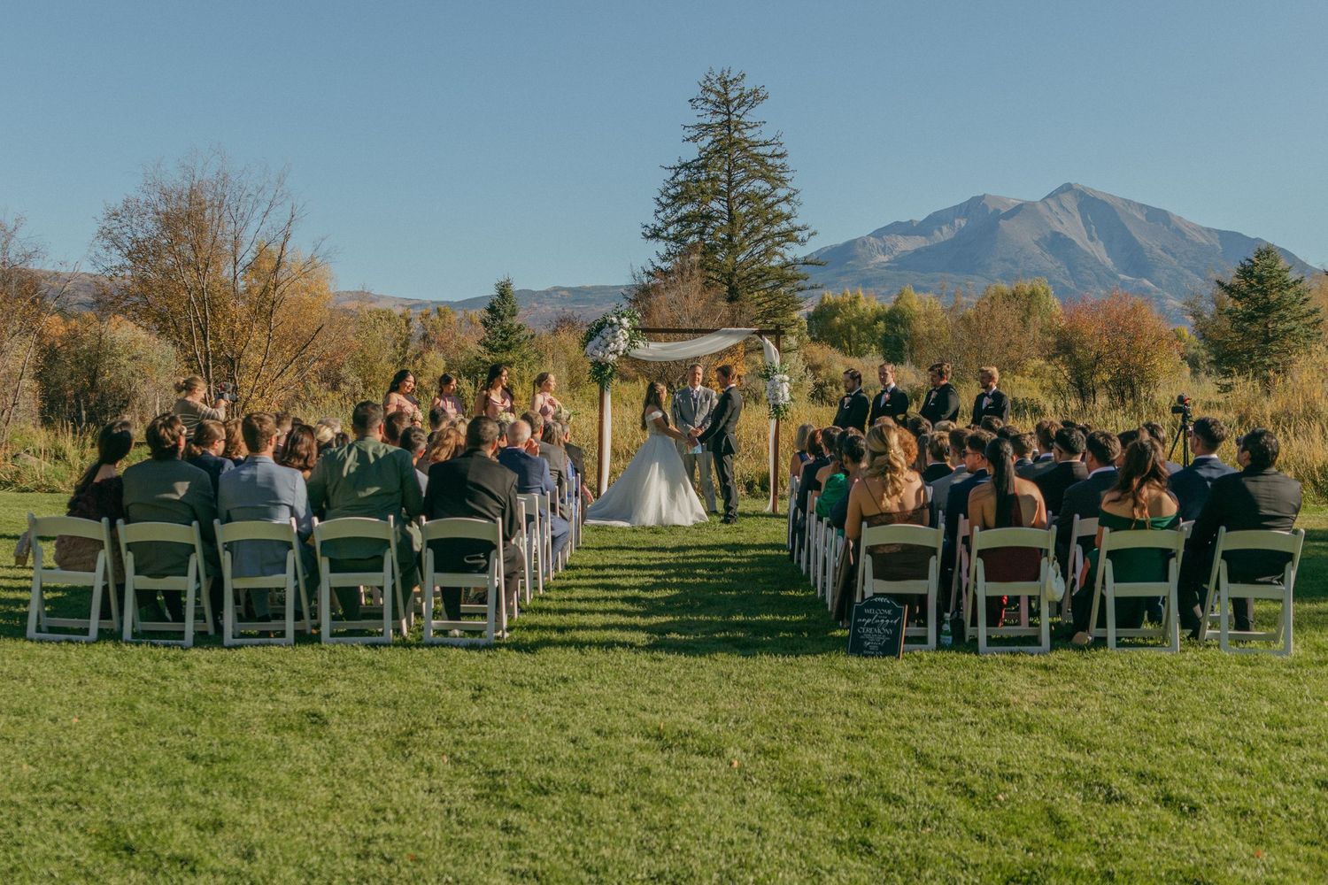 Outdoor wedding ceremony setup with rows of chairs on green grass facing mountain views in the distance.
