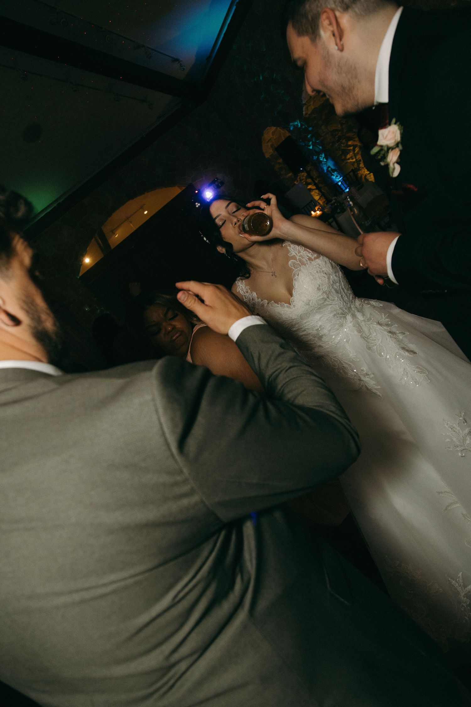 Bride in white gown laughs joyfully while dancing with guests at a lively wedding reception.