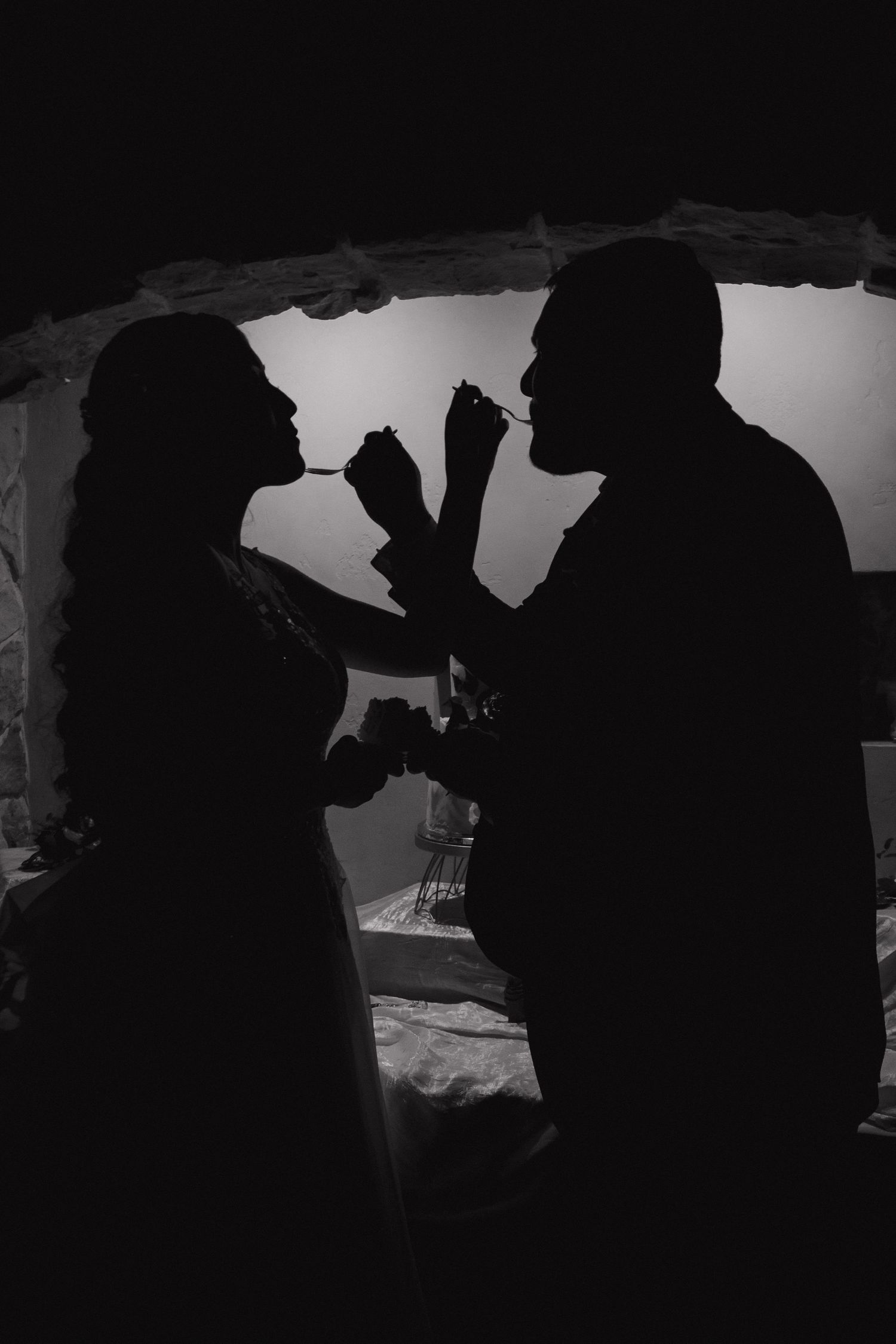 Silhouette of bride and groom sharing cake cutting moment in black and white.