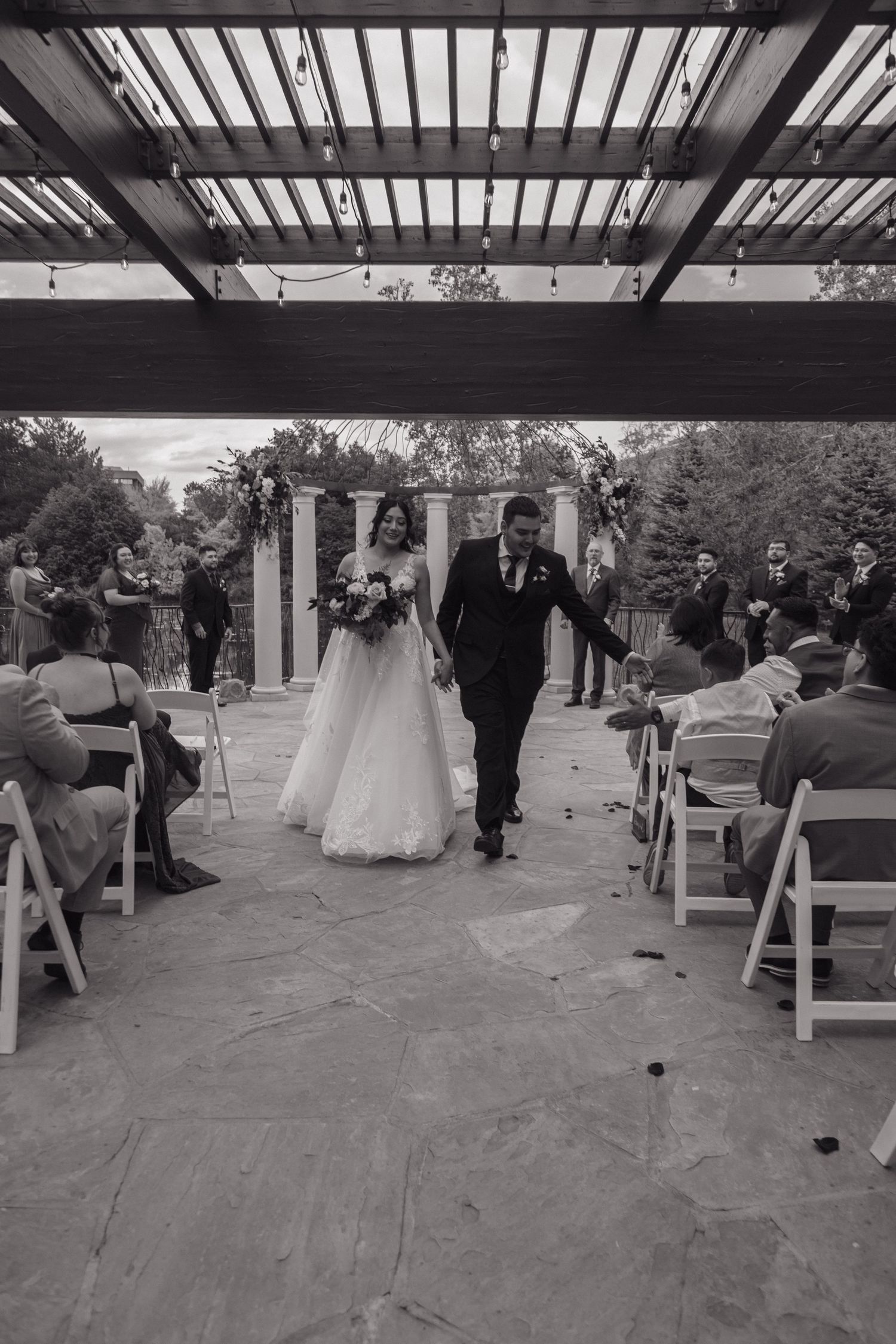 Black and white photo of newlyweds joyfully walking back down the aisle after their outdoor wedding ceremony.
