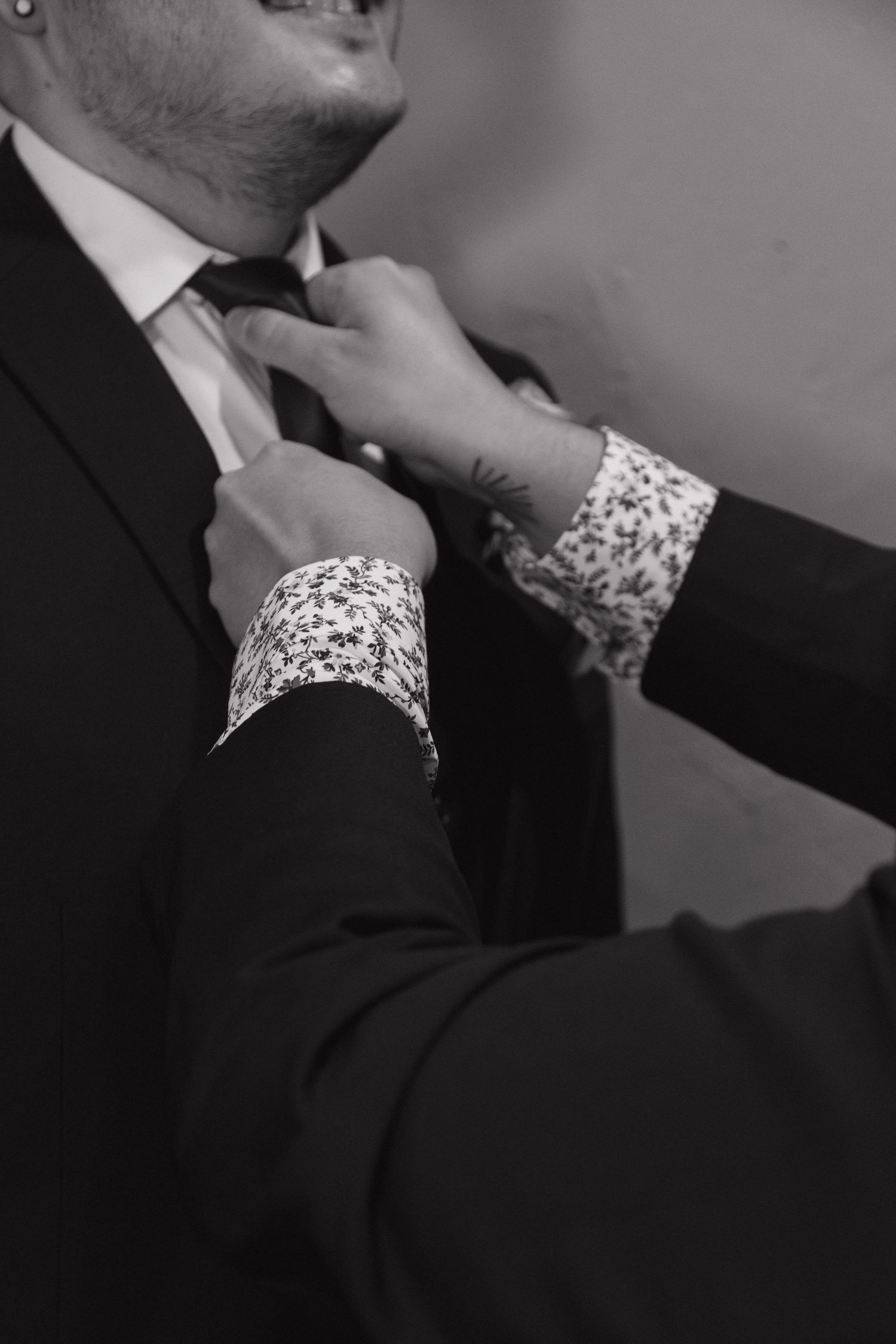 Groomsman adjusting groom's tie in black and white wedding preparation photo.