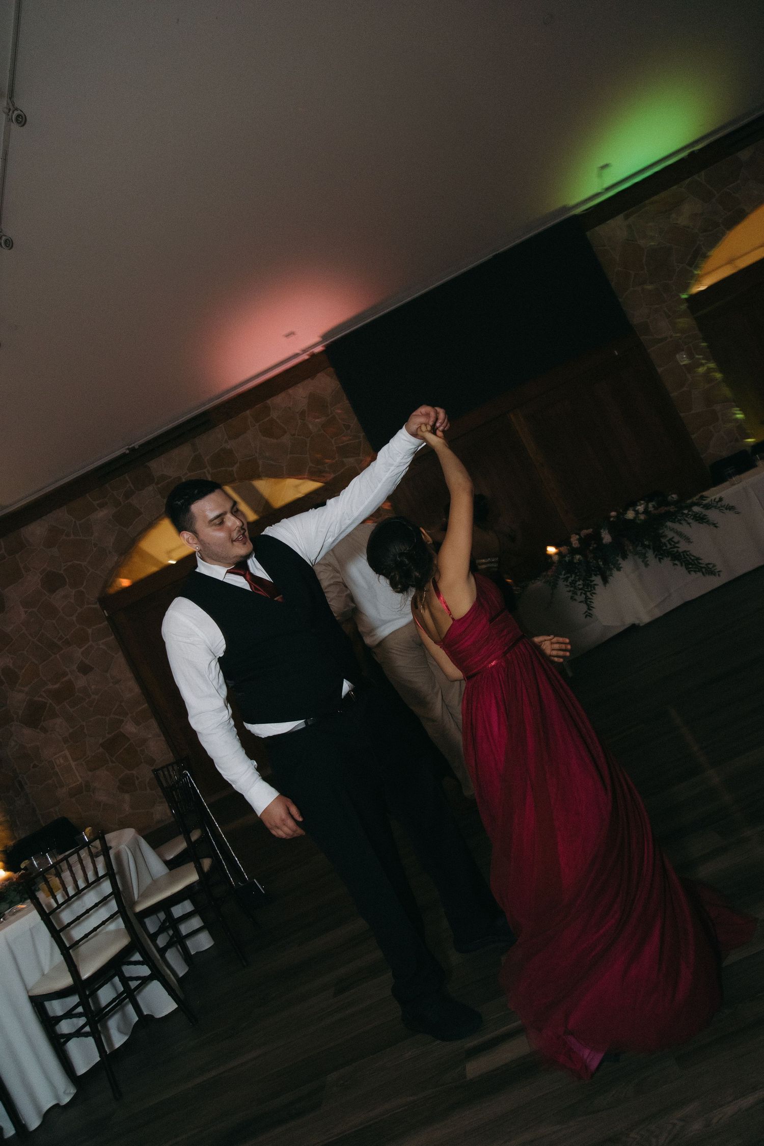 Groom spins bridesmaid in red gown during a lively wedding reception dance.