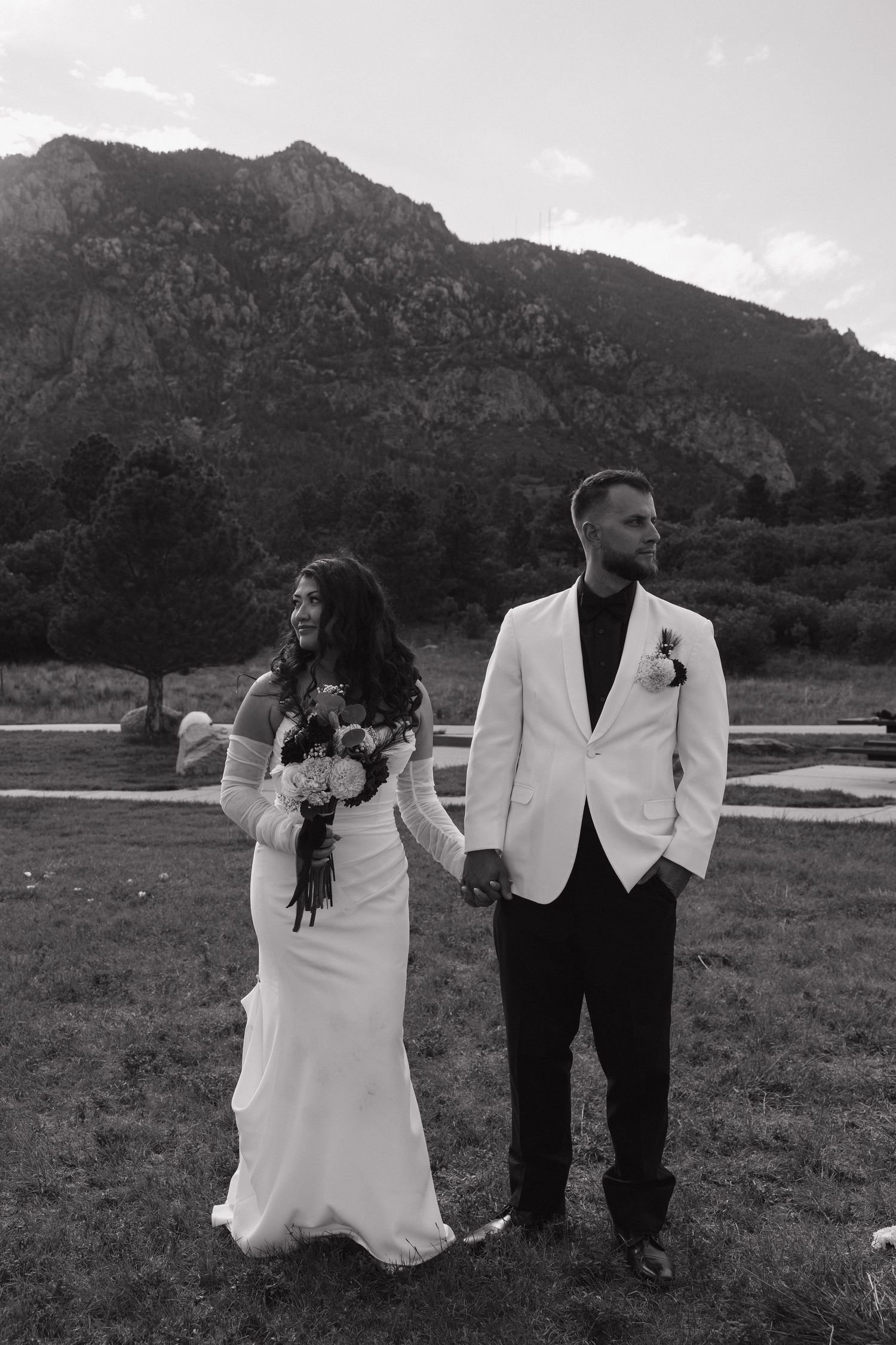 Black and white photo of bride and groom holding hands with mountain scenery behind them.