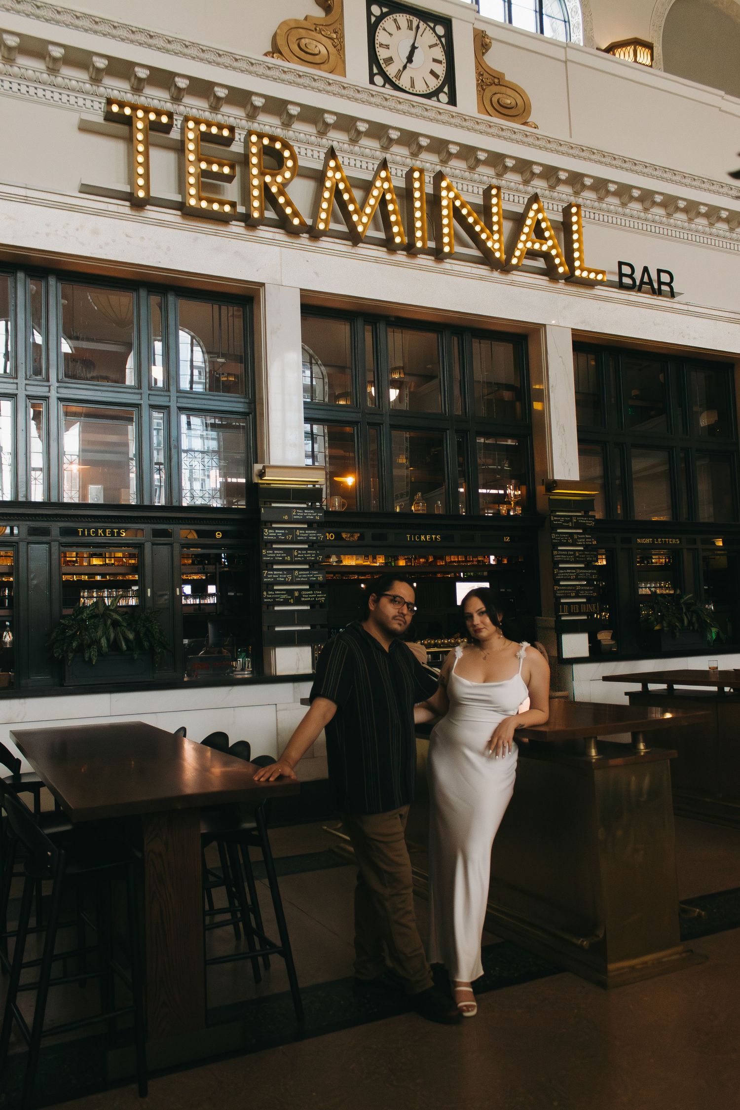 Couple standing together at the Terminal Bar, featuring vintage marquee lighting and elegant white interior decor.