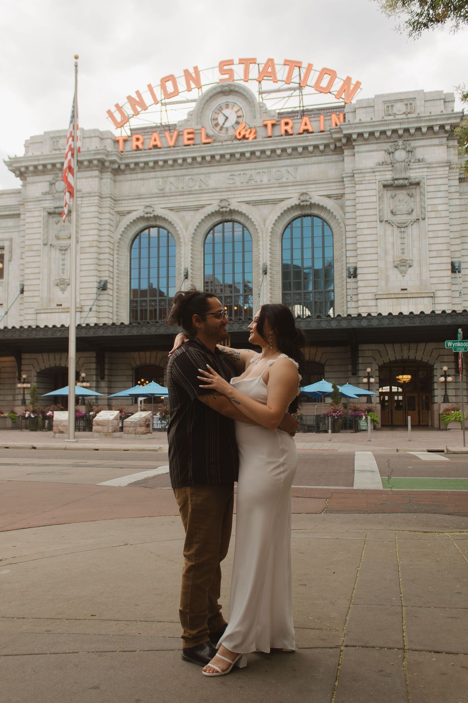 A couple embraces in front of the historic Union Station building in Denver with its iconic neon signage.