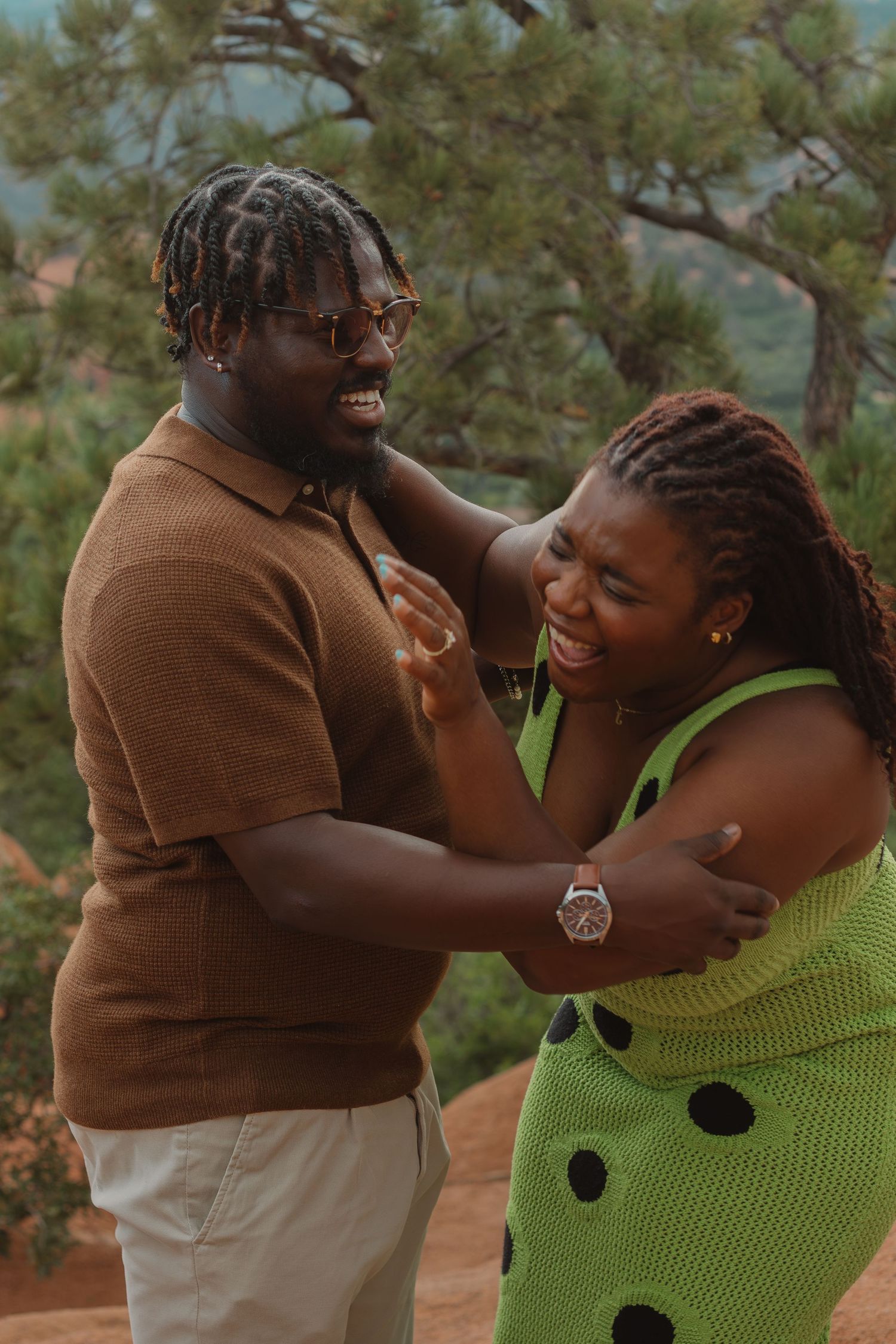 Joyful couple sharing an intimate moment wearing brown and green polka dot outfits against mountain scenery.