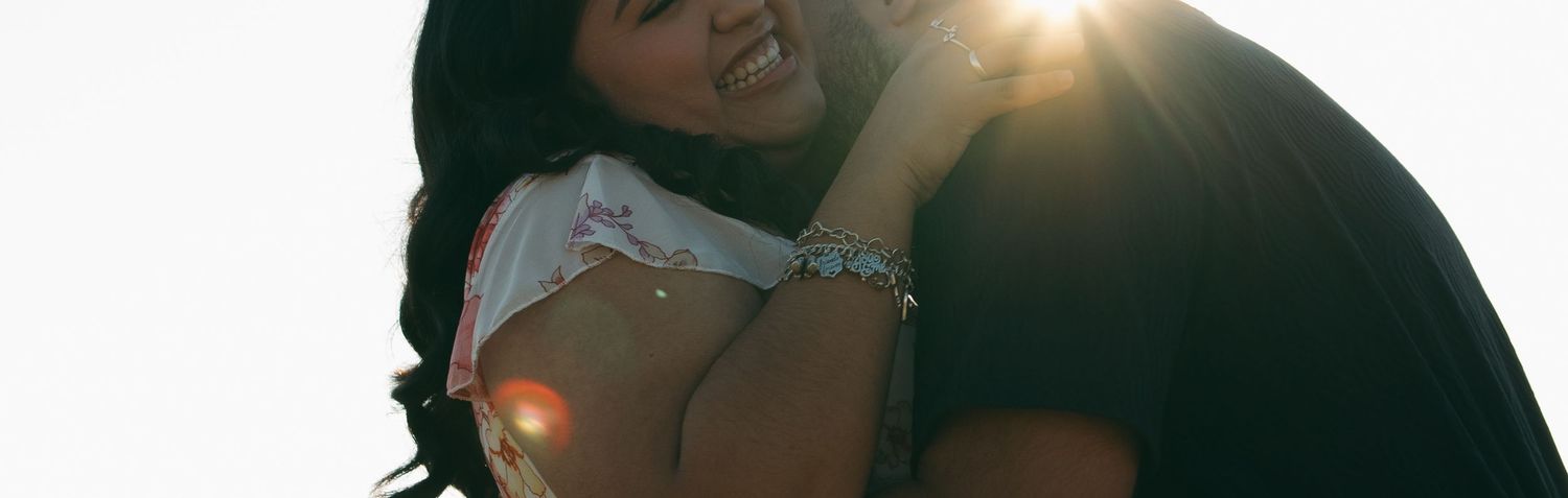 A couple embraces in a backlit outdoor setting creating a warm silhouette against sunlight.