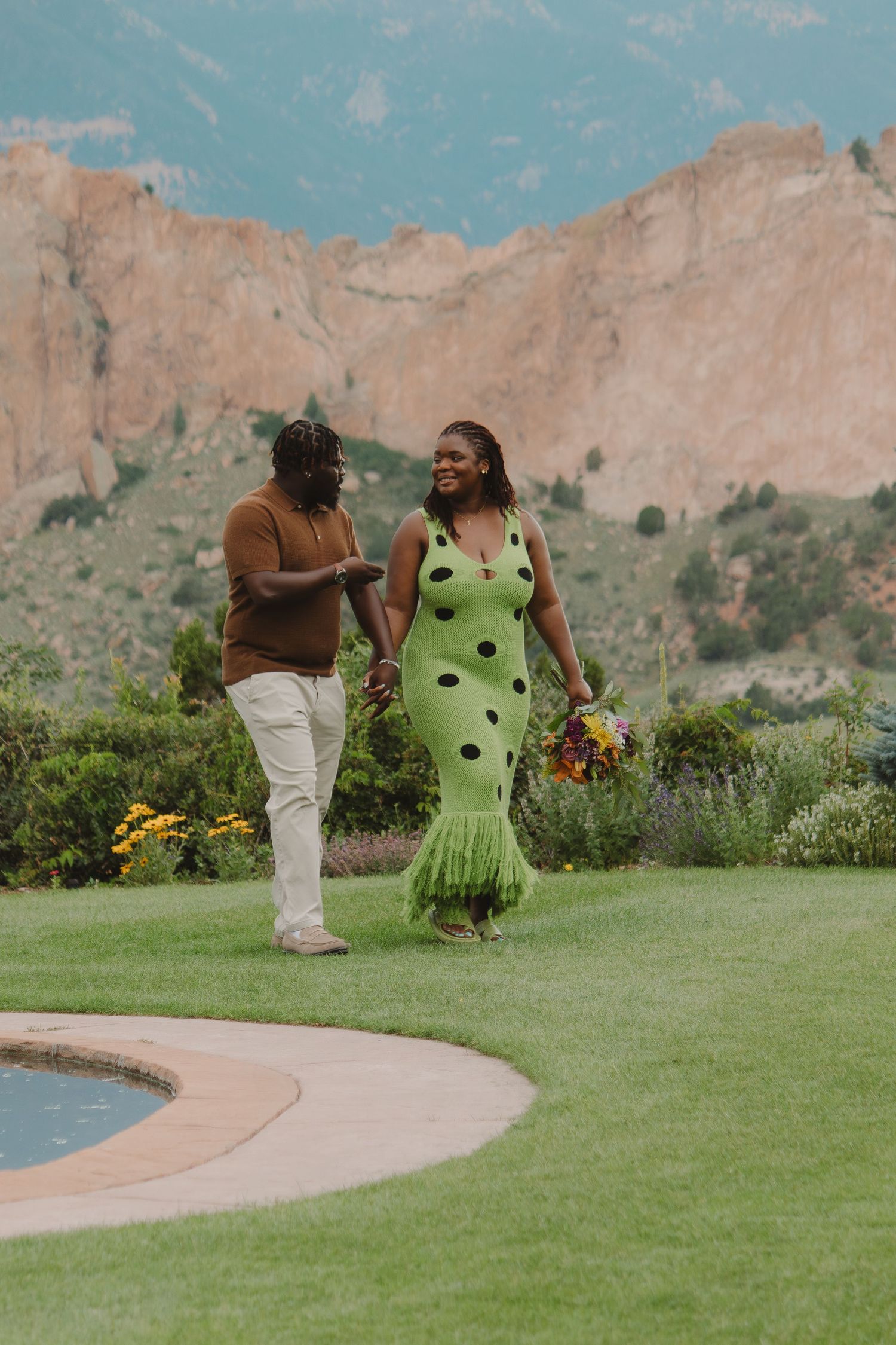 A couple shares an intimate moment together on a grassy lawn with red rock formations in the background at Garden of the Gods.