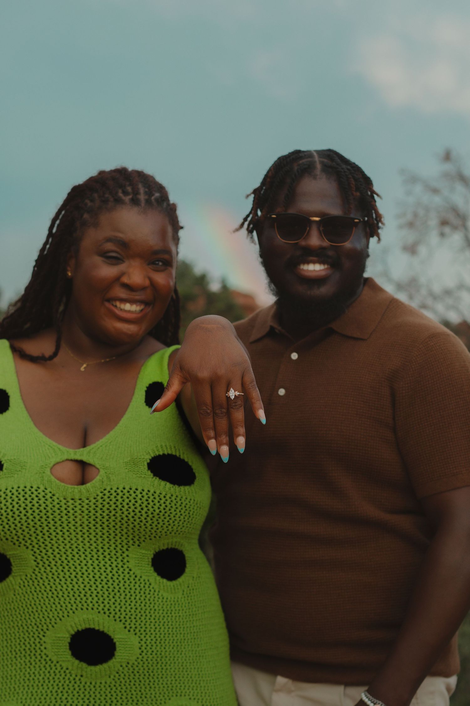 Happy couple posing outdoors with bright green polka dot dress and brown polo.