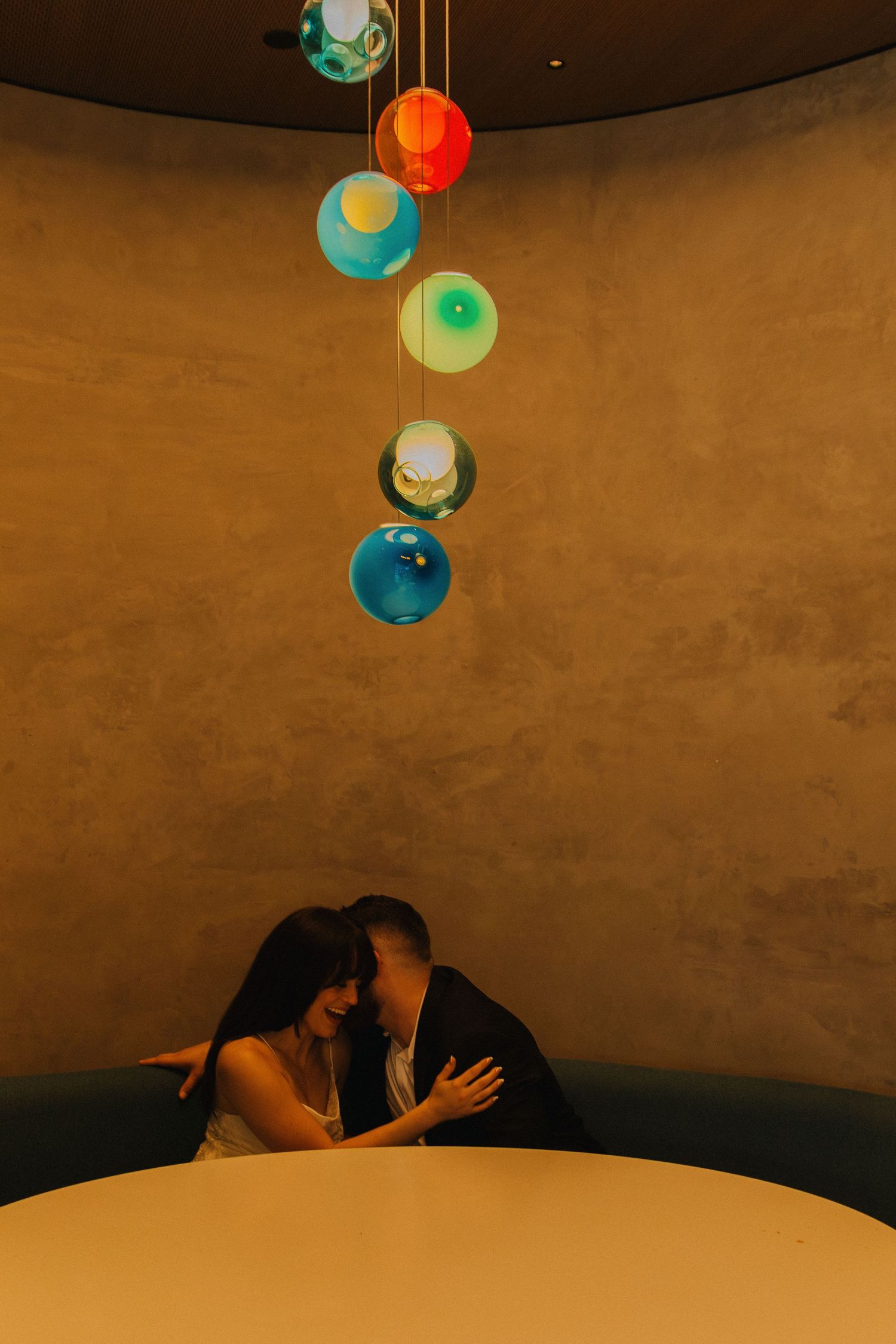 Couple shares intimate moment under colorful hanging spherical lights in dimly lit room.