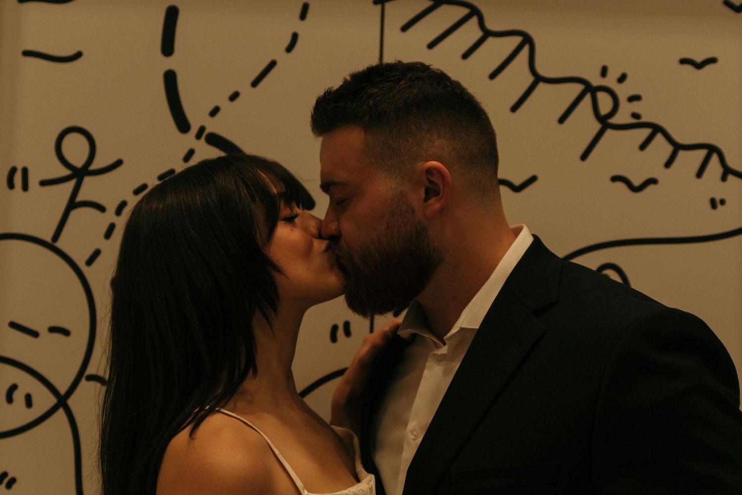A romantic moment shared between a couple against a wall with artistic doodle designs.