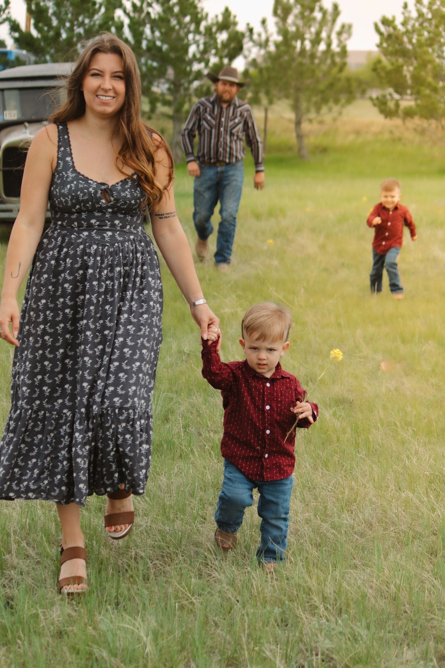 Family enjoying a casual photoshoot in a grassy field with a vintage car in the background.