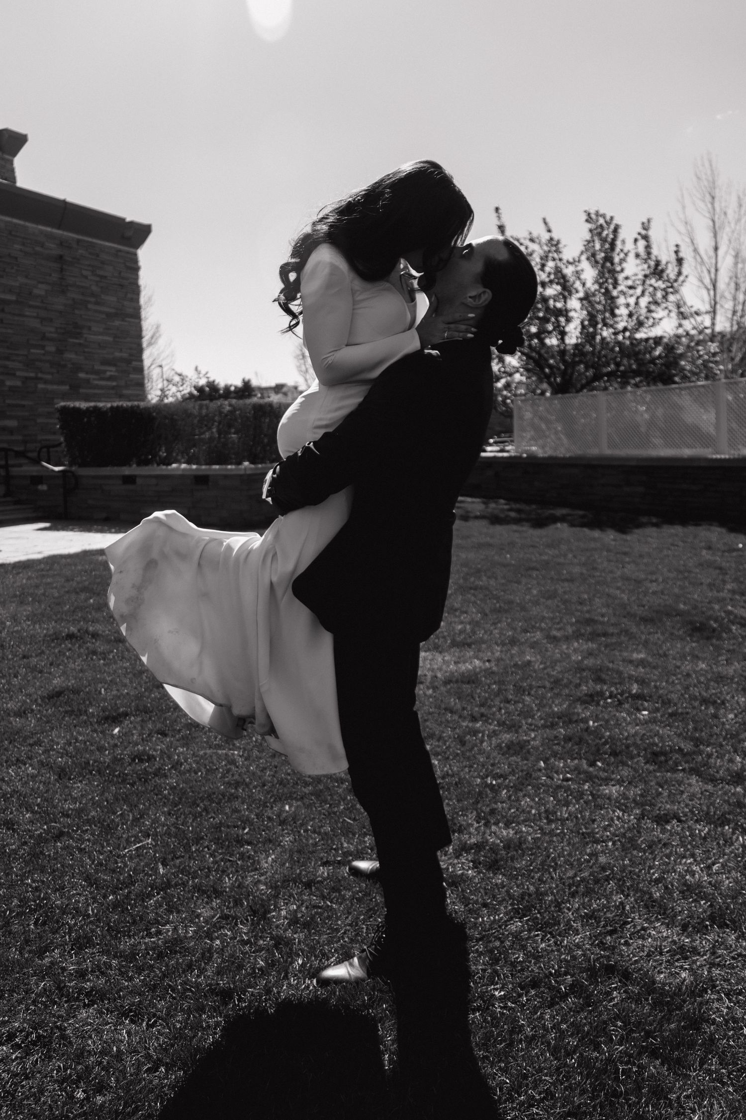 Black and white photo of groom lifting bride in the air for a kiss on a sunny lawn.