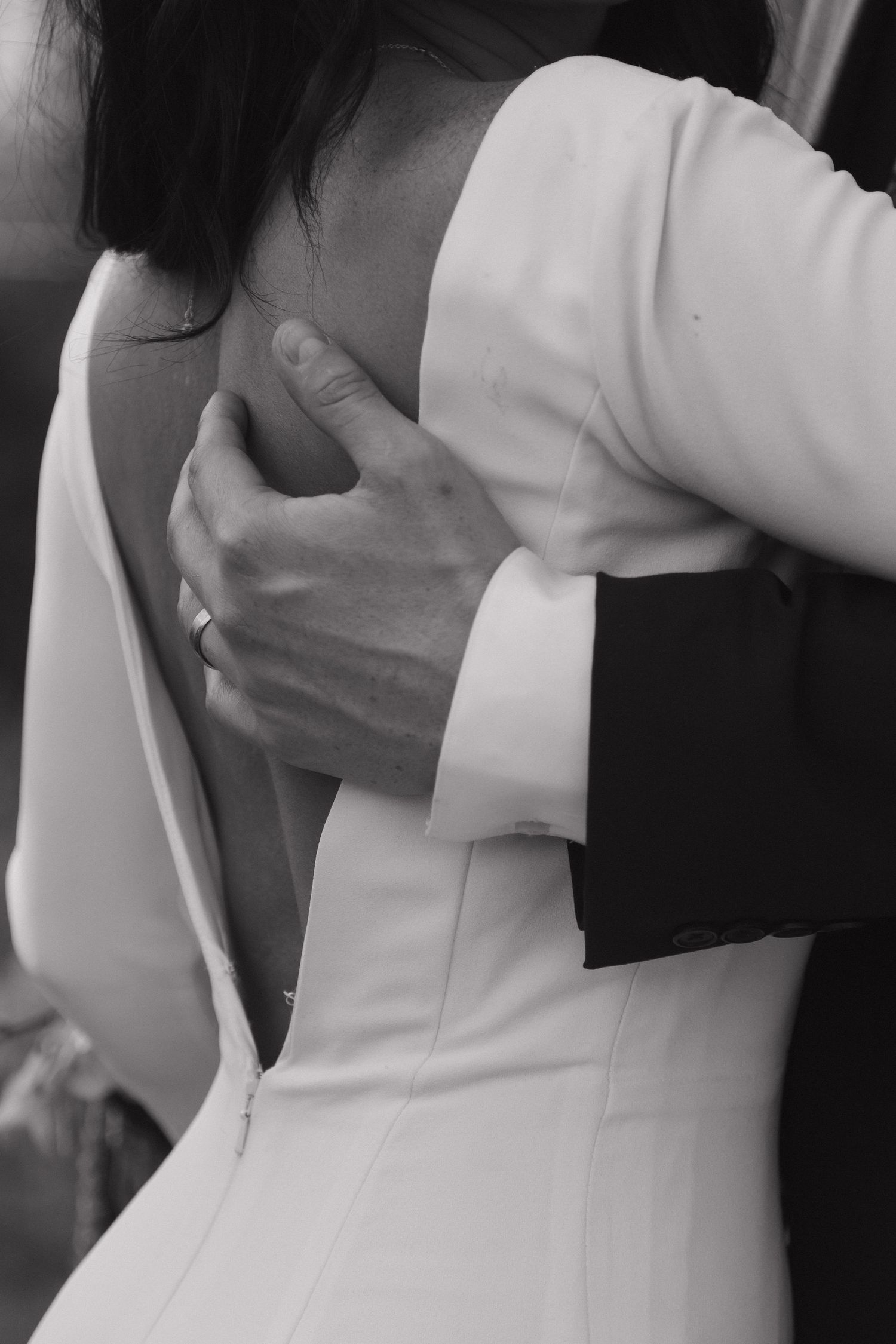 Black and white close-up of groom embracing bride in backless white wedding dress.