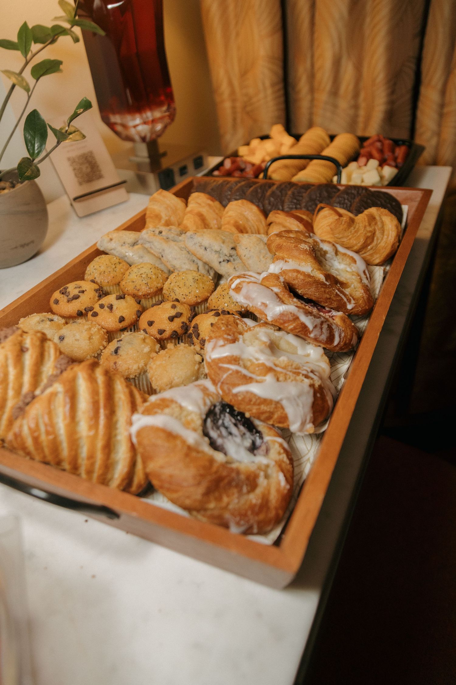 Wooden tray filled with assorted pastries, croissants, danishes, and cookies on a white tablecloth at a catered event.