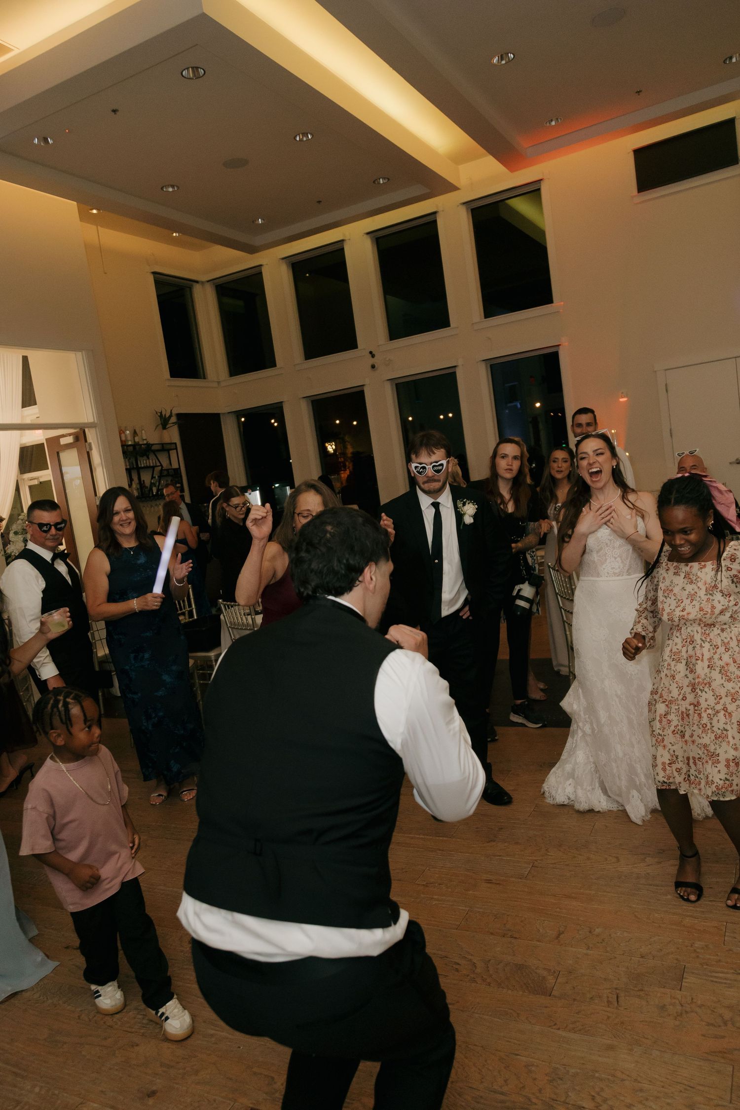 Lively wedding reception dance floor with guests celebrating around bride and groom in elegant venue.