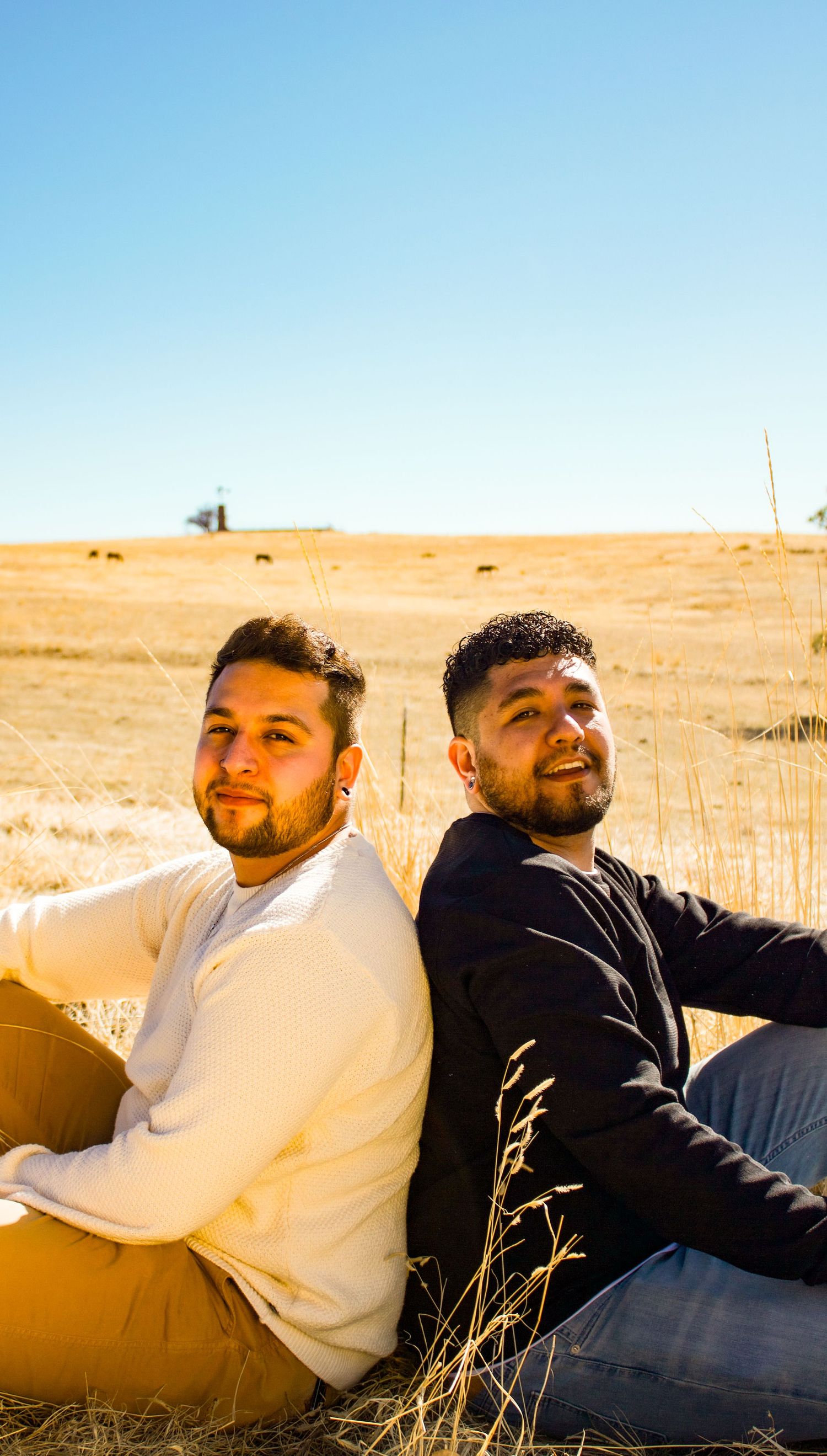 Two people sitting back-to-back in a golden field on a sunny day.