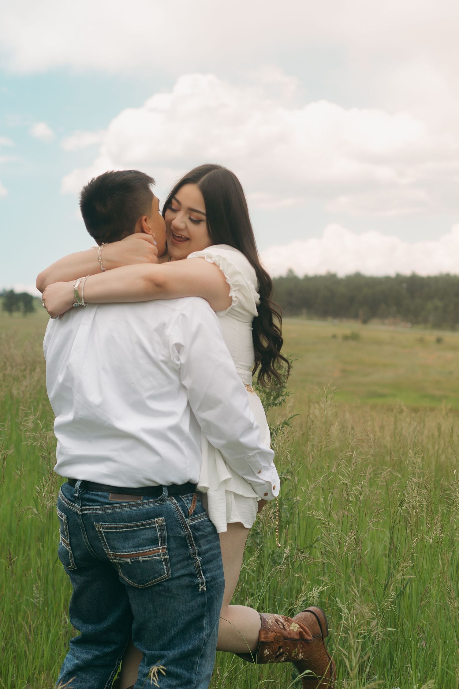 Sweet embrace in meadow with white clothing and rustic cowboy boots.