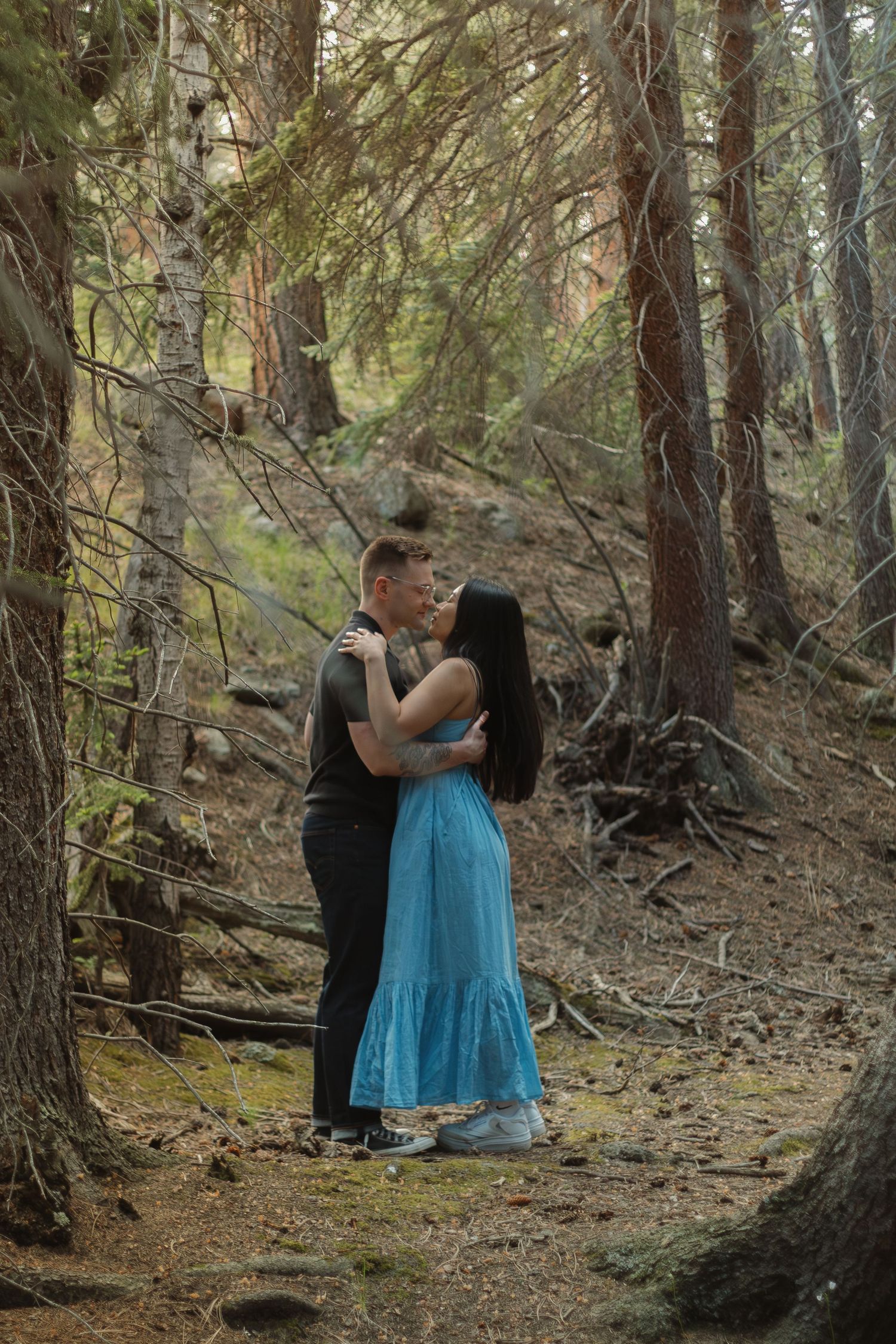 A romantic moment captured between two people in a woodland setting with filtered sunlight.