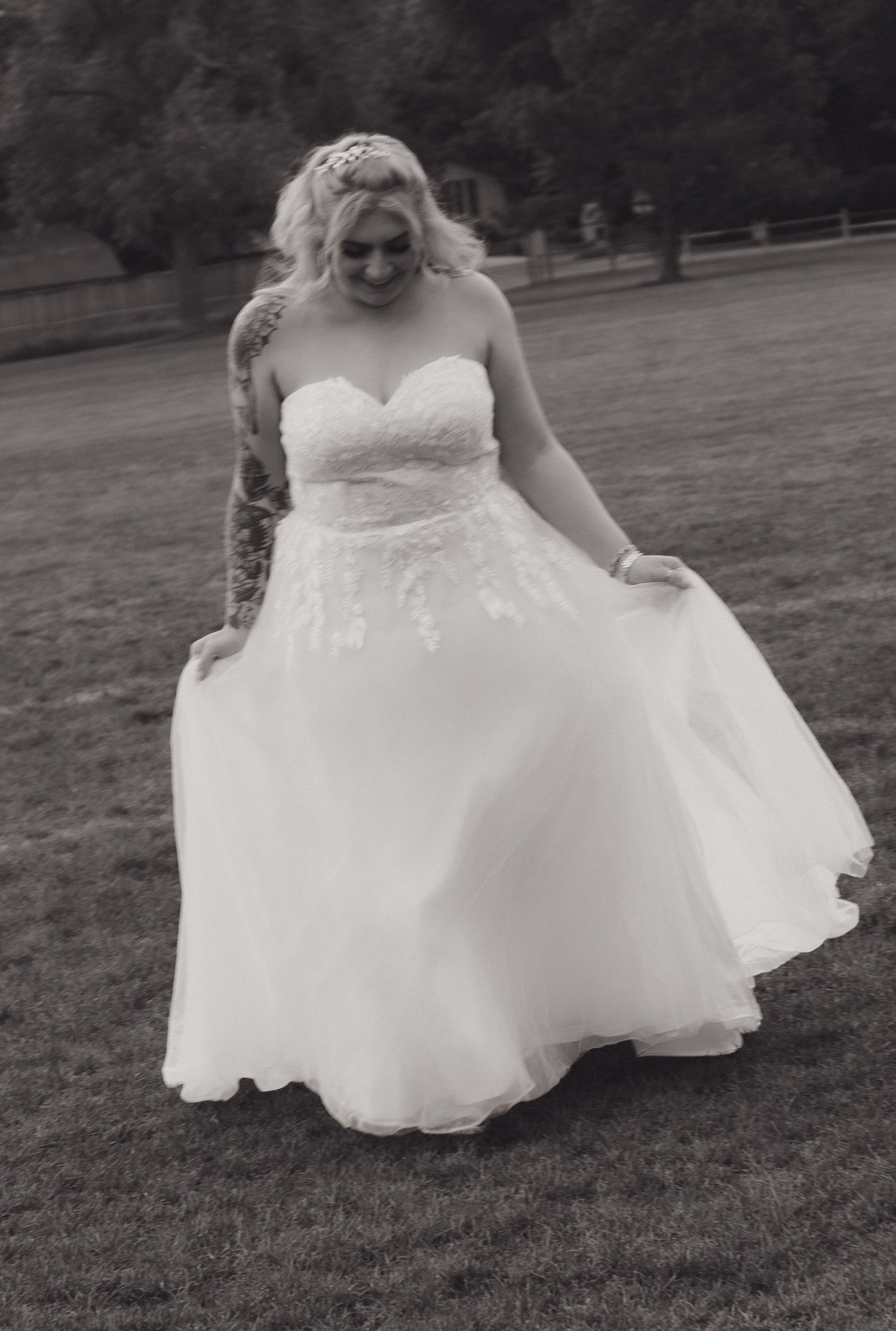 Black and white photo of wedding dress movement against grassy field backdrop.